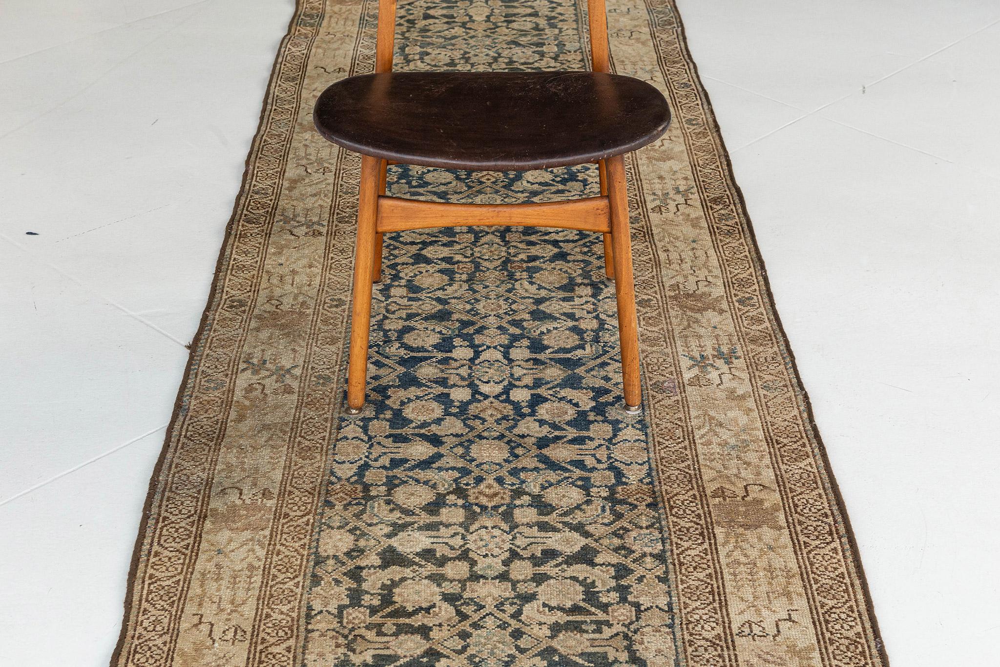 Un ravissant chemin de table ancien de style persan Malayer qui présente des motifs floraux dynamiques qui s'étendent gracieusement sur le champ abrasé. Entouré de bordures composées de bandes de garde à méandres floraux, ce tapis affiche un impact