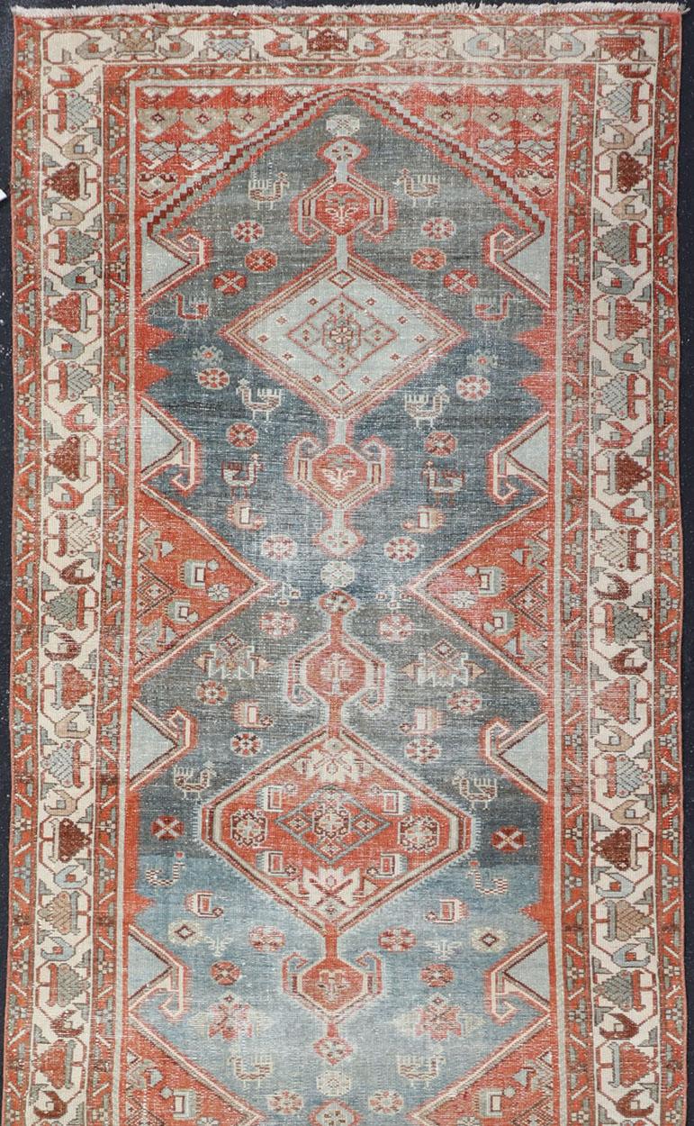 This antique Persian Malayer runner was hand-knotted in early 20th century and features a geometric medallion design replete with various motifs and is enclosed within a complementary, multi-tiered border. Rendered in blue, gray, cream, brown, burnt