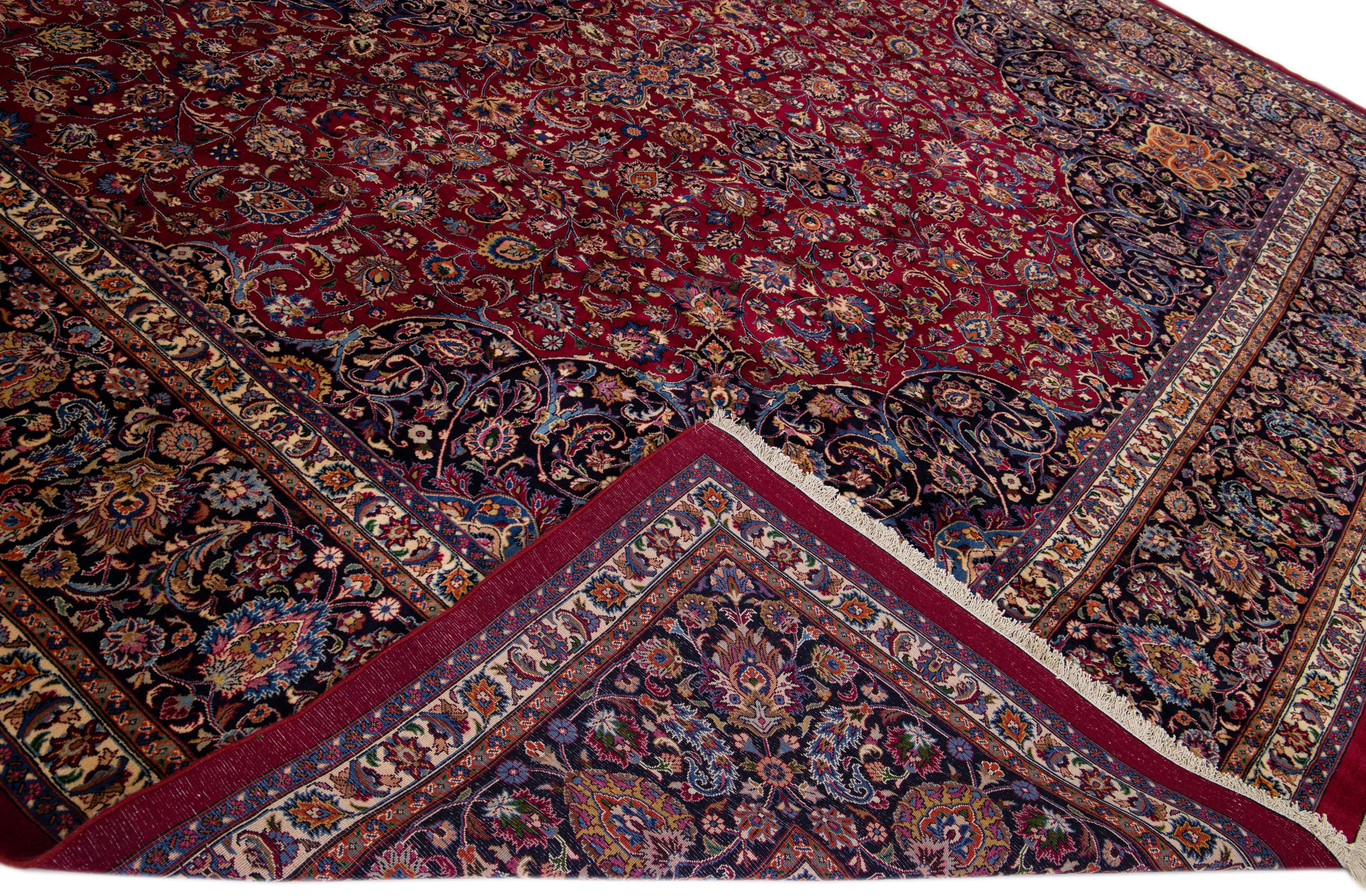 Beautiful Antique Mashad hand-knotted wool rug with a red field. This piece rug has a dark blue-designed frame With multicolor accents in a gorgeous all-over classic rosette design. 

This rug measures 13'4