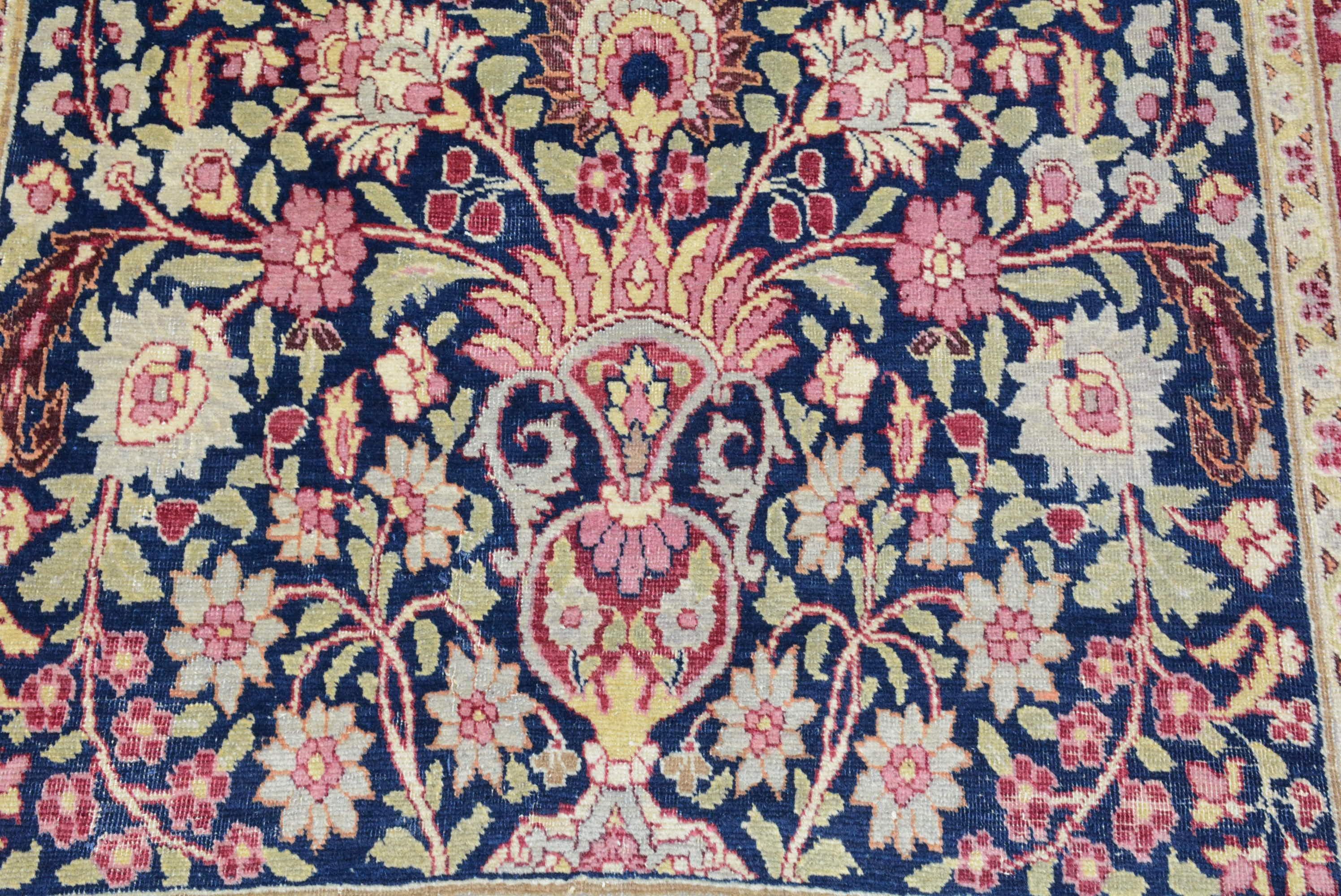 An ascending floral pattern fills the midnight blue field of this early 20th century Mashad rug from east Persia, 5' 7