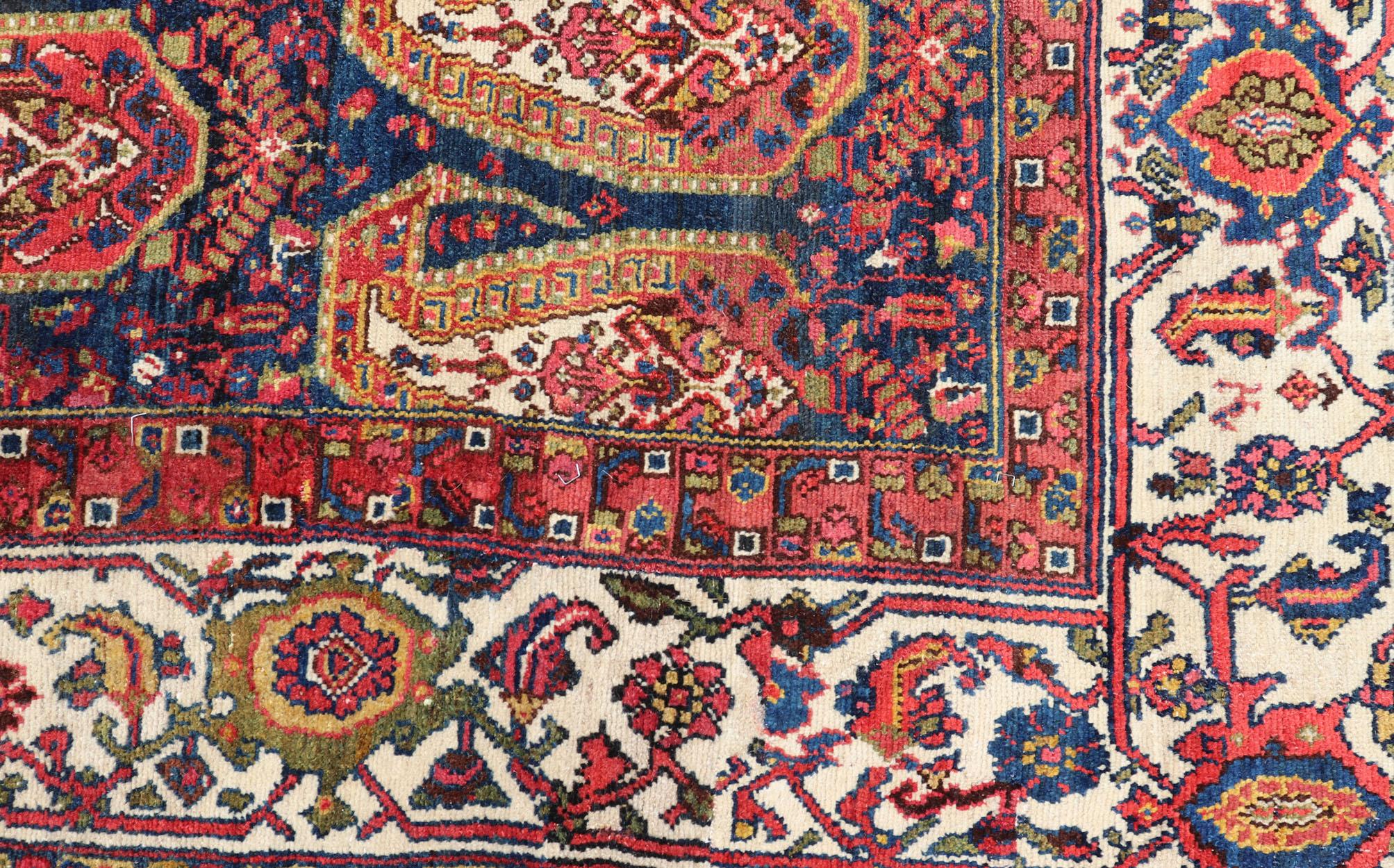This unique Persian Hamadan features a dark blue background placed behind a sub-geometric, red and mustard paisley design. The boldened border highlights ivory between red, blue, olive, and hints of gold, hand woven in Northwestern Iran. 

Keivan