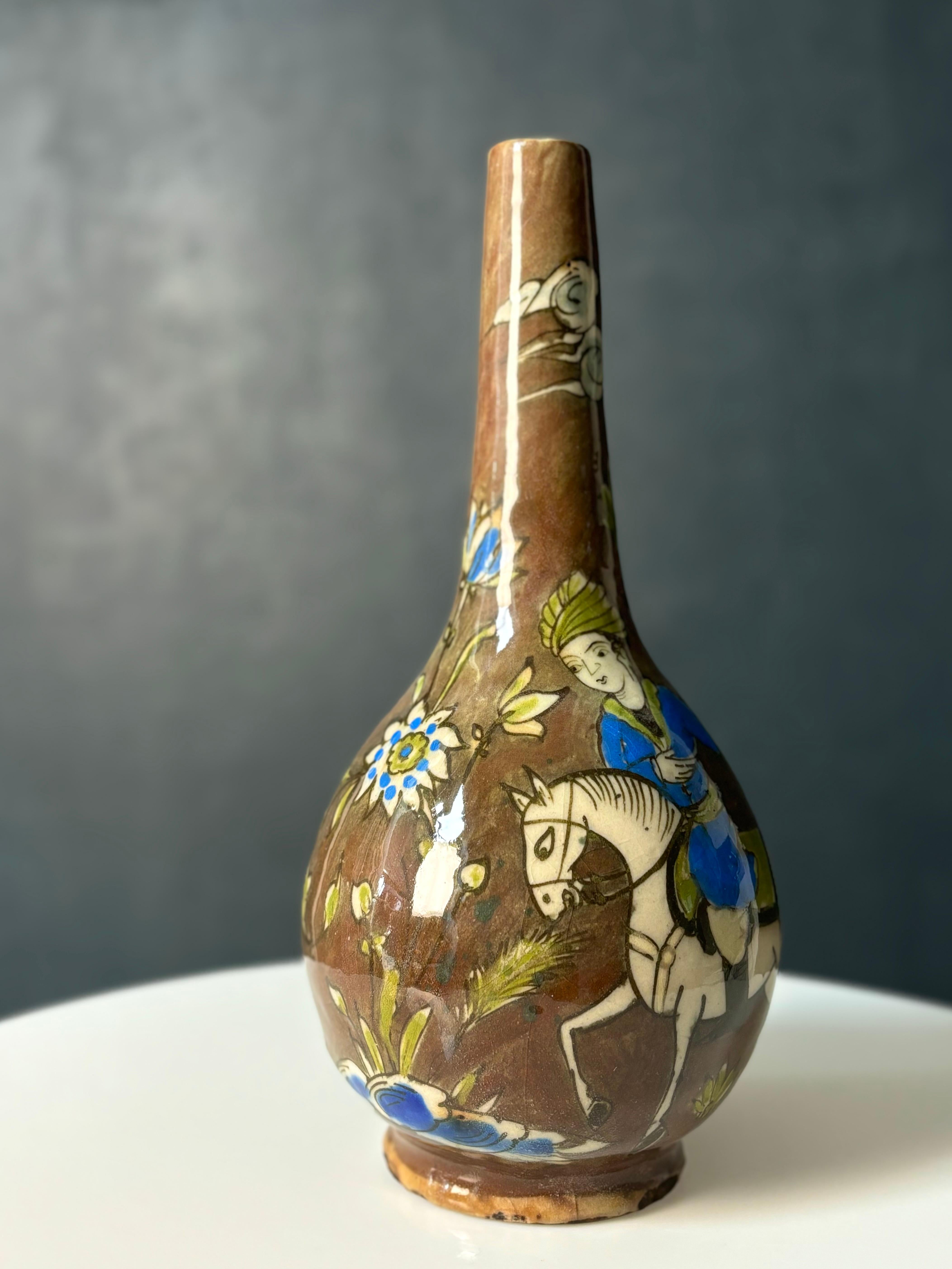 Grande vaso a bottiglia persiano del Medio Oriente con decorazioni organiche dipinte a mano che raffigurano persone, animali e fiori nei colori blu cobalto, bianco, verde e grigio tenue su uno sfondo marrone cedro lucido. 
Bellissime condizioni