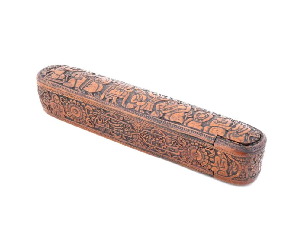 Un ancien plumier en bois persan Qajar sculpté à la main. La boîte a une forme allongée avec des coins arrondis. La partie supérieure du couvercle de la boîte représente une scène multifigurale, les côtés sont ornés de motifs floraux sculptés à la