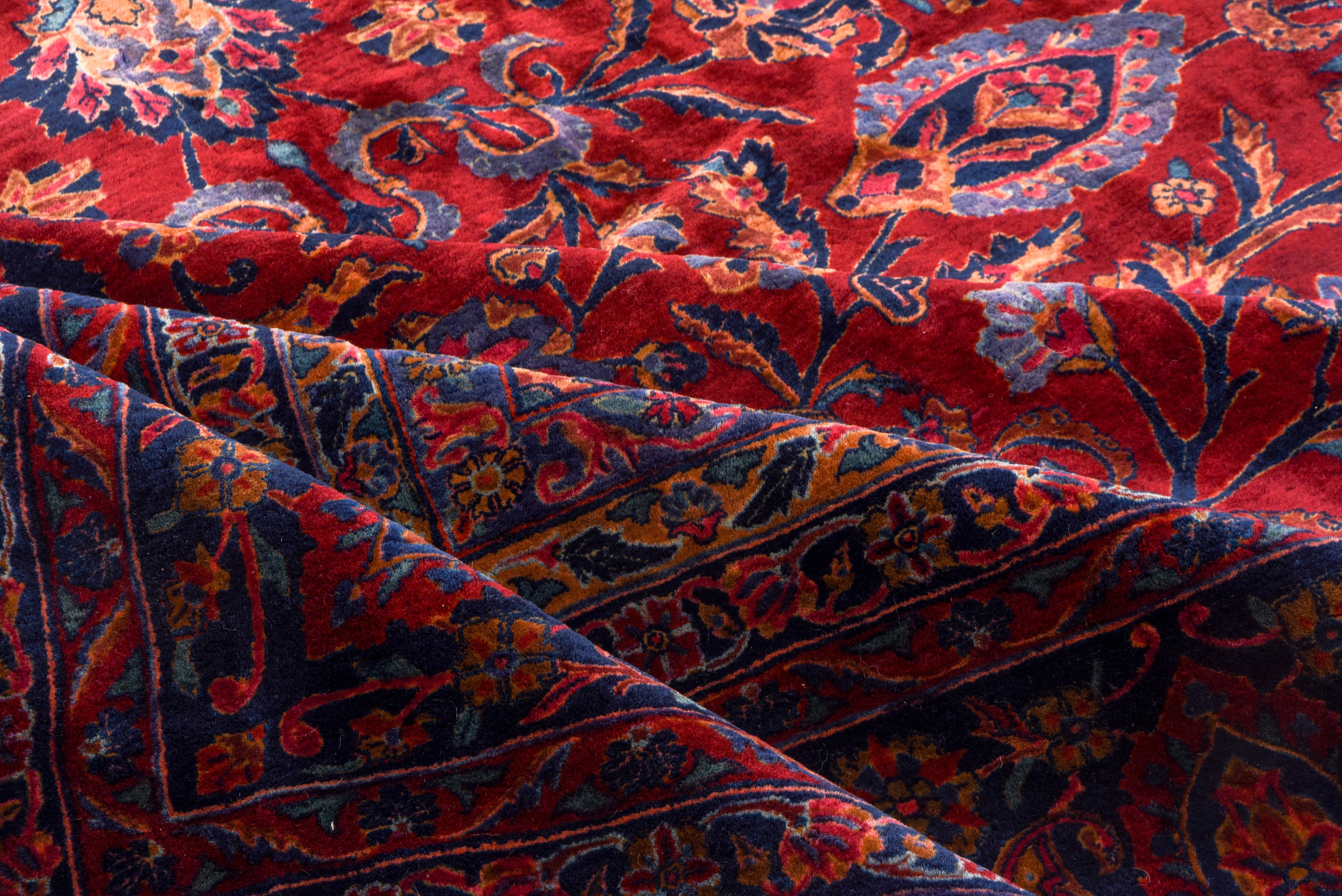 Ce tapis de ville de Perse centrale en laine filée à l'anglaise, de grande taille et en excellent état, reflète la palette rouge ou bleue contemporaine de Sarouk. Le champ rouge avec des bandes colorées et des palmettes, touchées en bleu clair, est