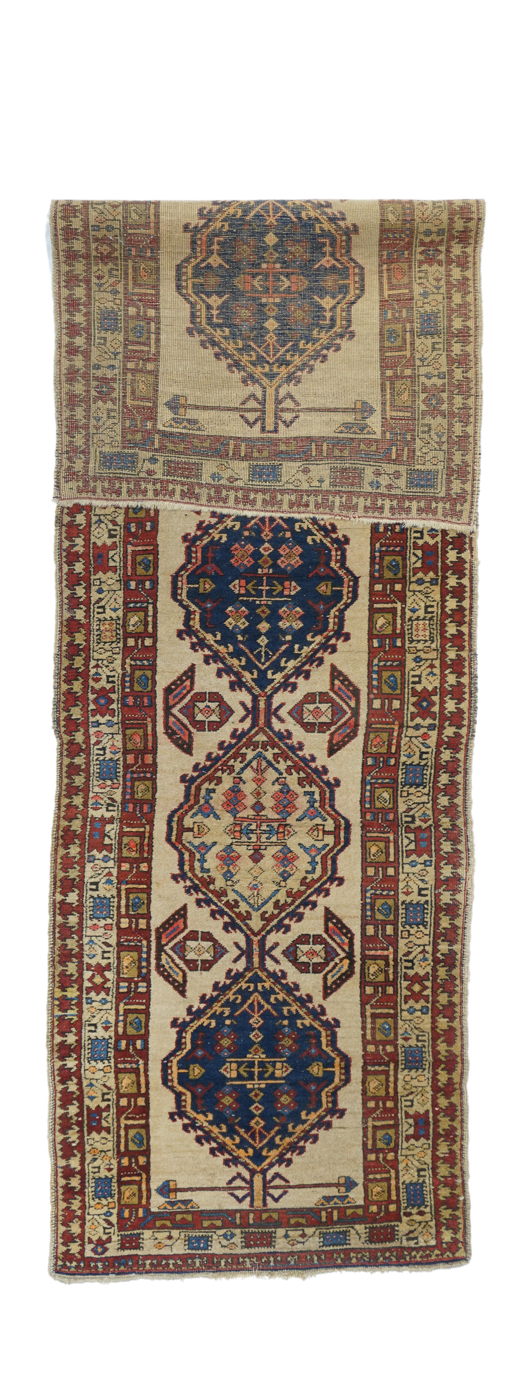 The milky camel field shows a pole medallion of five cartouches alternating in dark blue and straw, with hooked edges and stylized floral lateral fillers. Main border with fringed squares and formal stems, outer  Firm weave, medium weave.Red and