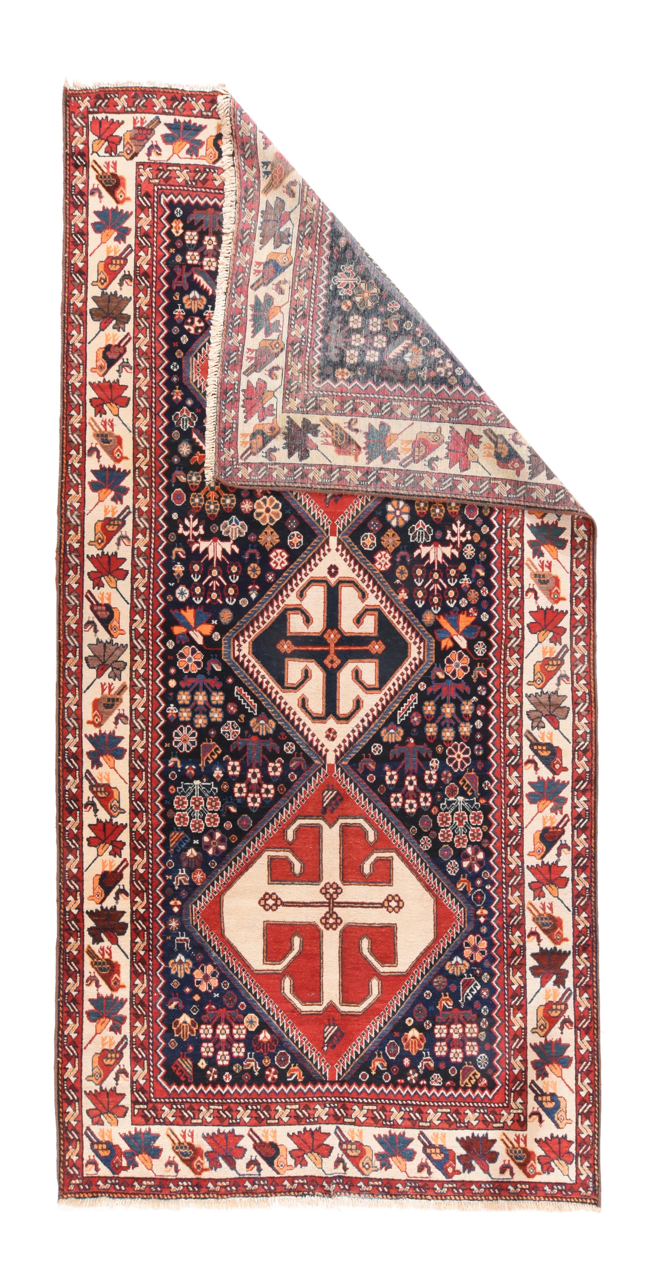 Tapis persan antique 5'3'' x 10'. Ce kellegi (long tapis) rustique présente un médaillon à trois sections en rouge et ivoire, avec des bords en dents de scie et des périphéries crochetées, sur un fond bleu marine étroitement parsemé de rosettes et