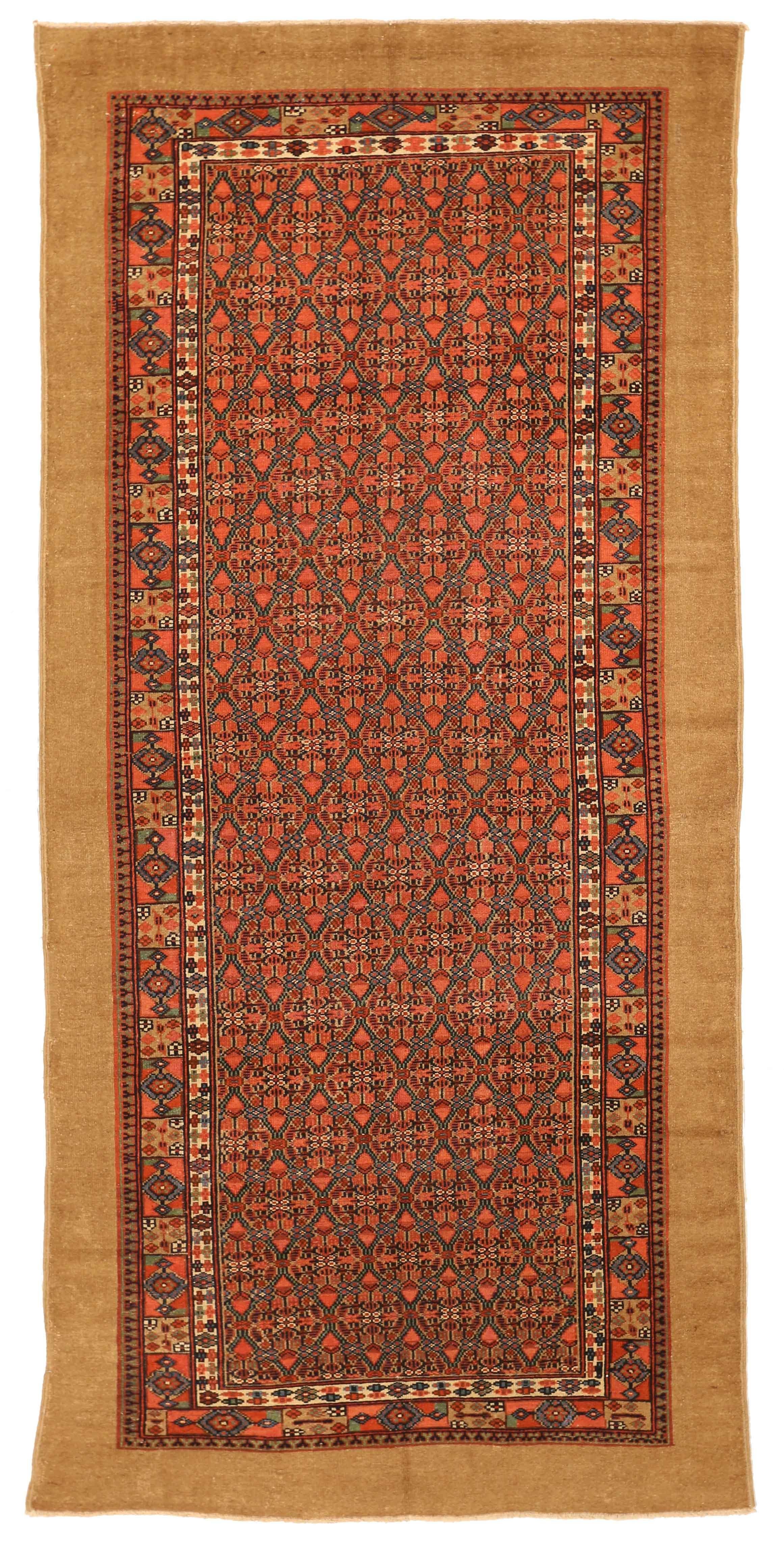 Handwoven from luxurious camel hair, this beautiful antique Persian rug features repeating geometric patterns in green and navy blue over an orange backdrop. Its simple appearance from afar belies the intricate details that can only be seen up