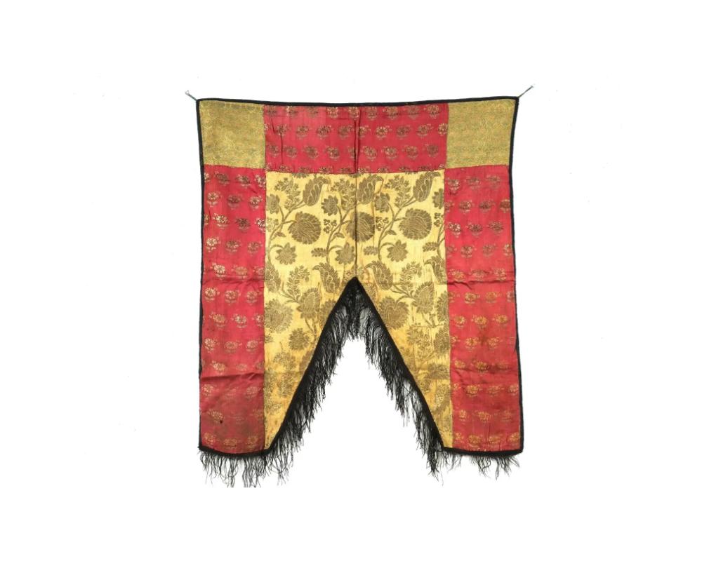 An antique Persian Iranian Safavid dynasty hand woven embroidered textile wall hanging. The textile is made in a fragment design, adorned with gold threaded floral and foliage ornaments. The ware is decorated with black fringes to the edge below.