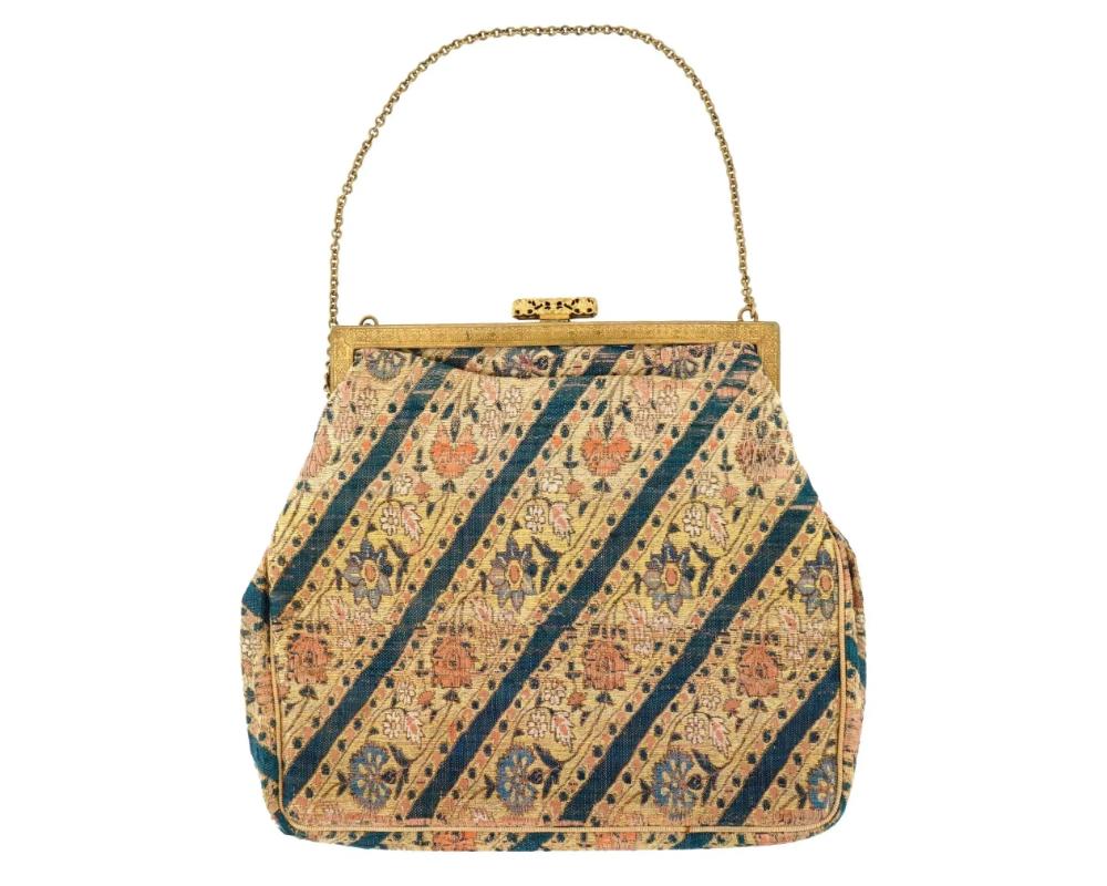 An antique Persian Safavid hand woven textile handbag clutch. ?irca 18th century. The textile is decorated with floral motifs on a beige background. The frame of the bag is gold tone and ornate. A delicate gold chain serves as the handle, enhancing