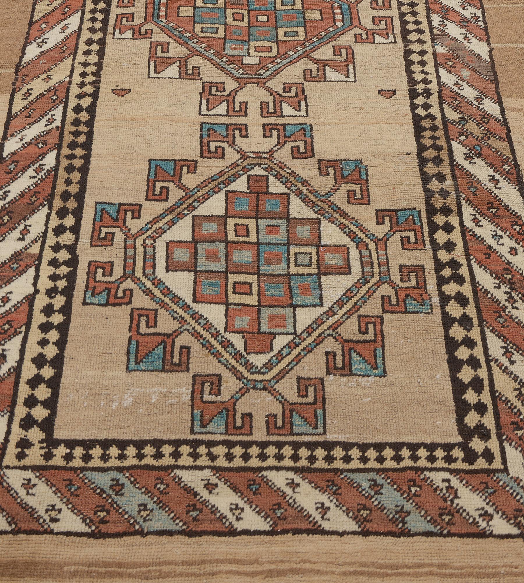 This antique, circa 1900, Serab runner has a sandy-brown field with a central column of six ivory hooked lozenges each containing stepped linked polychrome square panels, in a border of ivory, light blue and terracotta-red diagonal stripes between