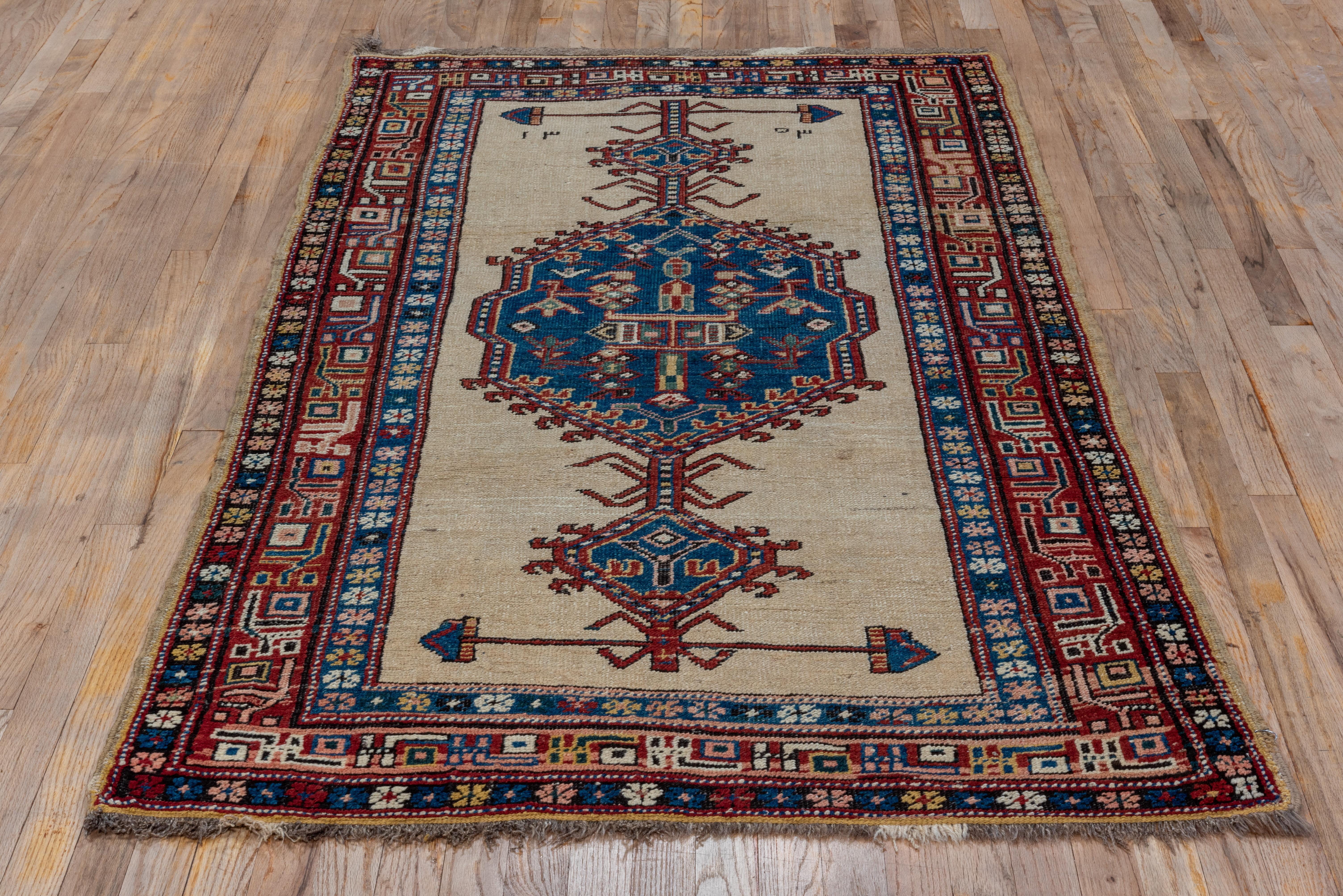 Rare in this dozar rug format, this NW Persian rustic scatter shows an ecru open field with on large, characteristic Serab medallion in blue, with pendants ending in double arrow horizontal finials. Narrow main red border of highly geometric