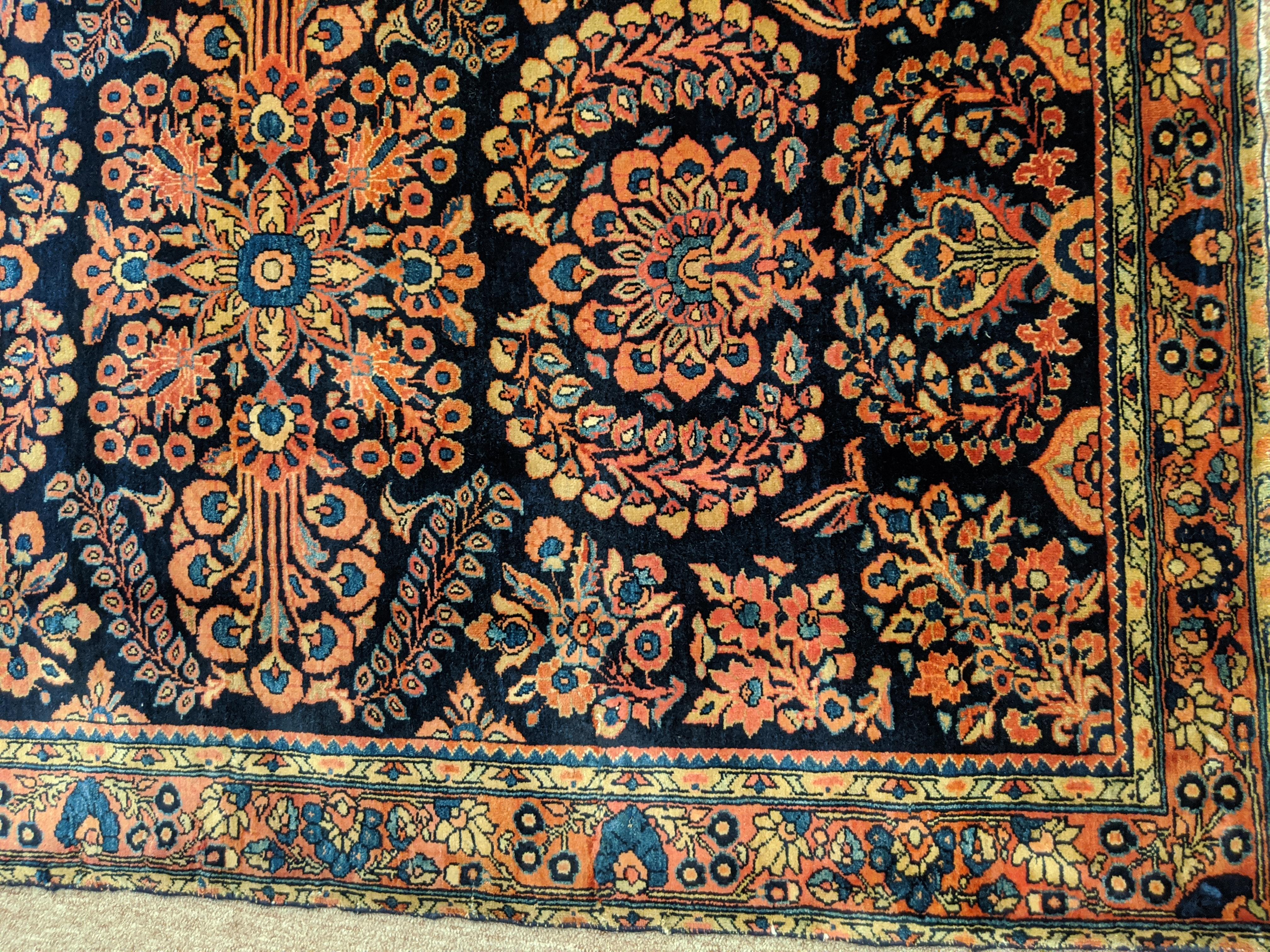 Persian Sarouk with an all-over field design with a navy background and a coral border. The field is decorated with vines, tendrils and flowers in light blue, gold and teal. The wool is so soft that it feels like silk, circa 1920. It is 3-3 x 4-10.