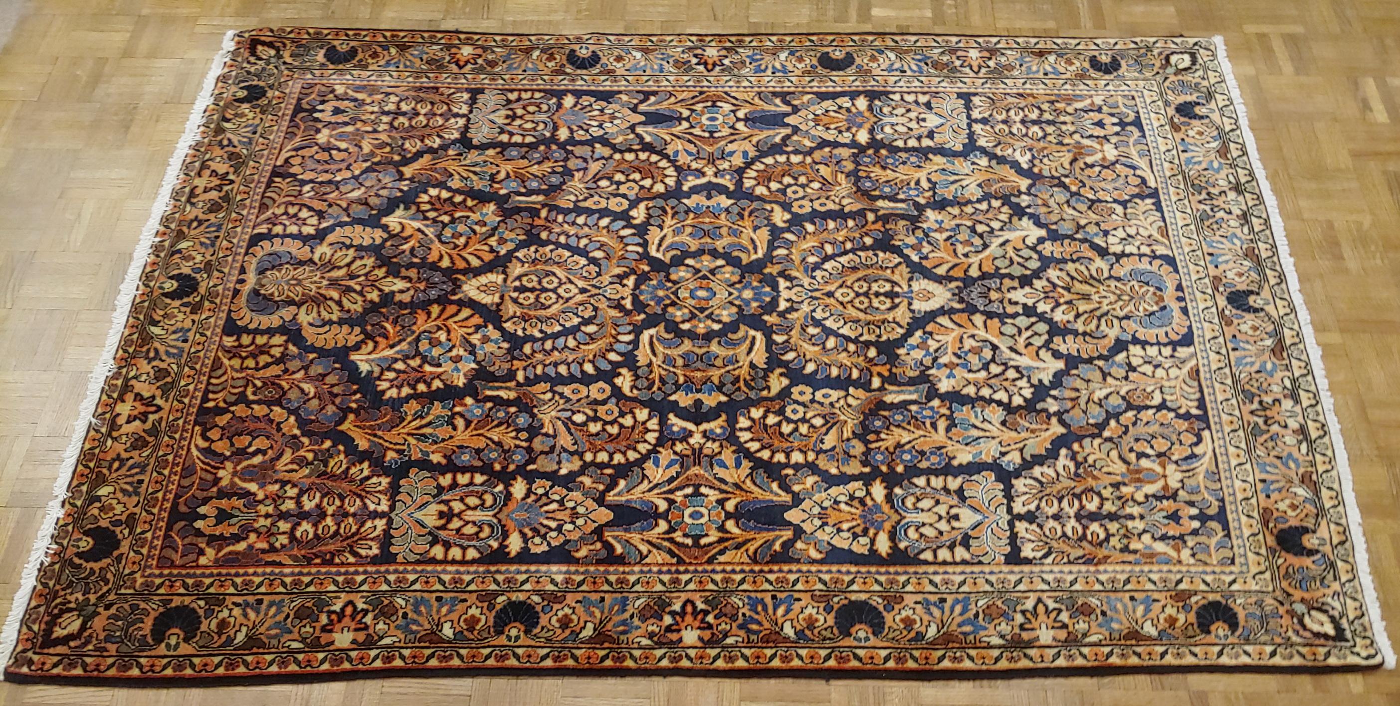 Persian Sarouk with an all-over field design with a navy background and a coral border. The field is decorated with vines, tendrills and flowers in light blue, gold and teal. The wool is so soft that it feels like silk. It is 4-3 x 6-3, circa 1920.
