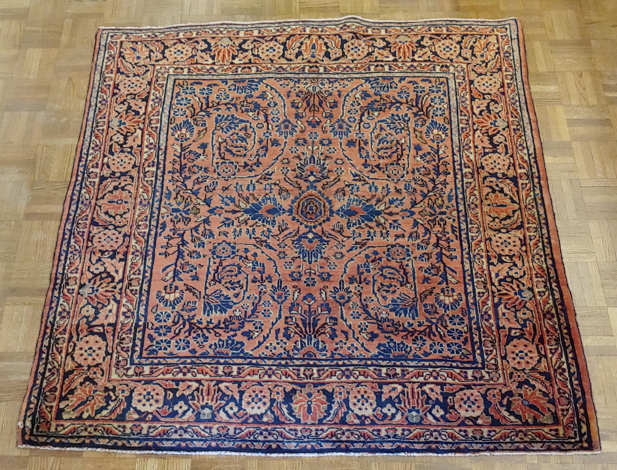 Persian Sarouk with an all-over field design with a rust background and a navy border. The field is decorated with vines, tendrills and flowers in light blue, gold and teal. The wool is so soft that it feels like silk. It is a square size 4-5x4-9