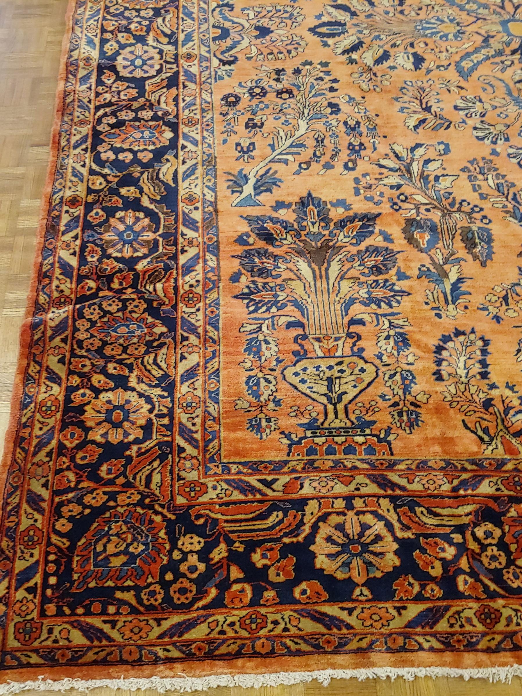 Persian Sarouk with an all-over field design with a rust background and a navy border. The field is decorated with vines, tendrills and flowers in light blue, gold and teal. The wool is so soft that it feels like silk. It is 9 x 11-9, circa 1920.