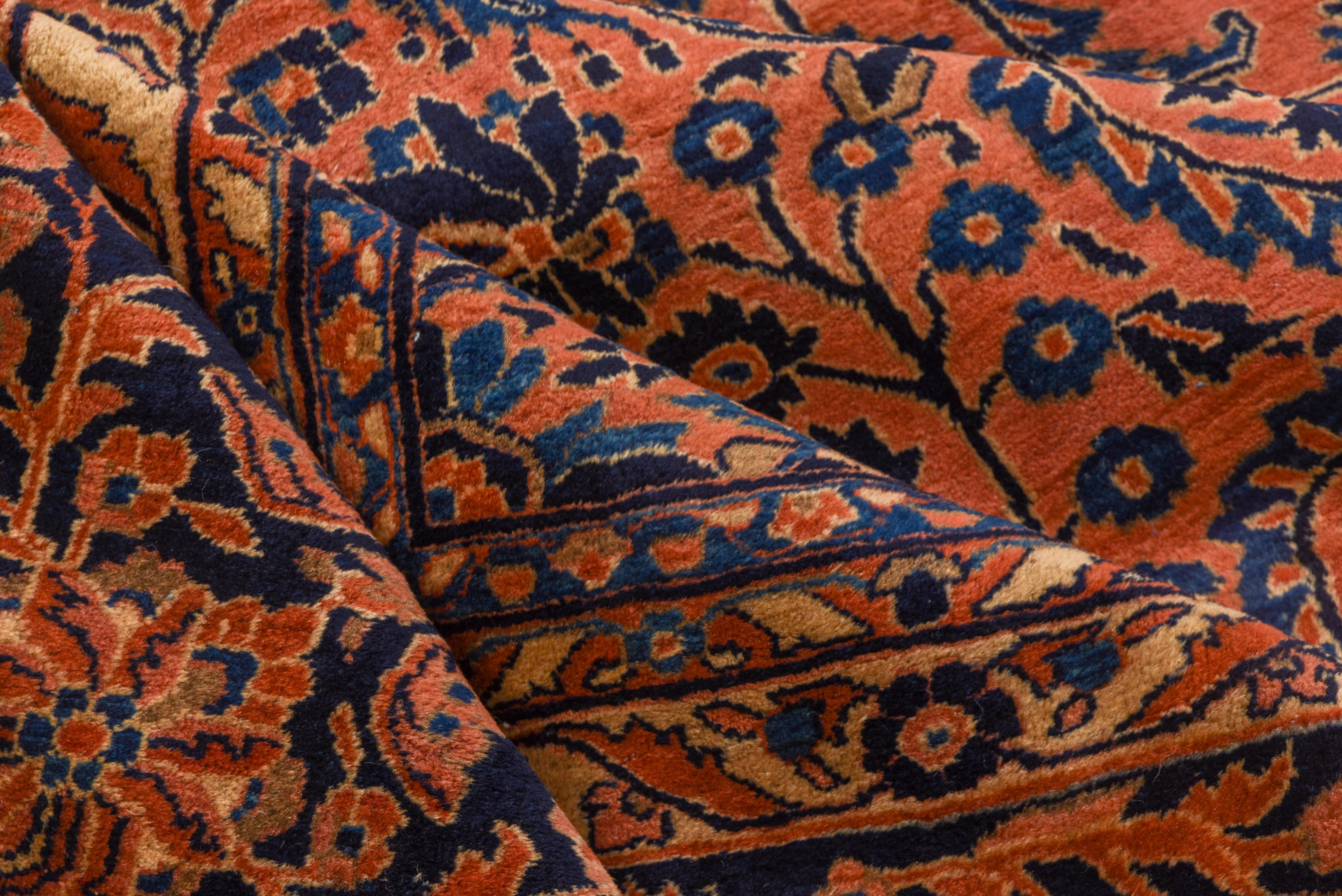 This is a Classic example of the incredibly popular west Persian Sarouk carpets made almost exclusively for the American market. The rosy orange field shows a close all-over pattern of closely set floral sprays accented in various blue tones. The