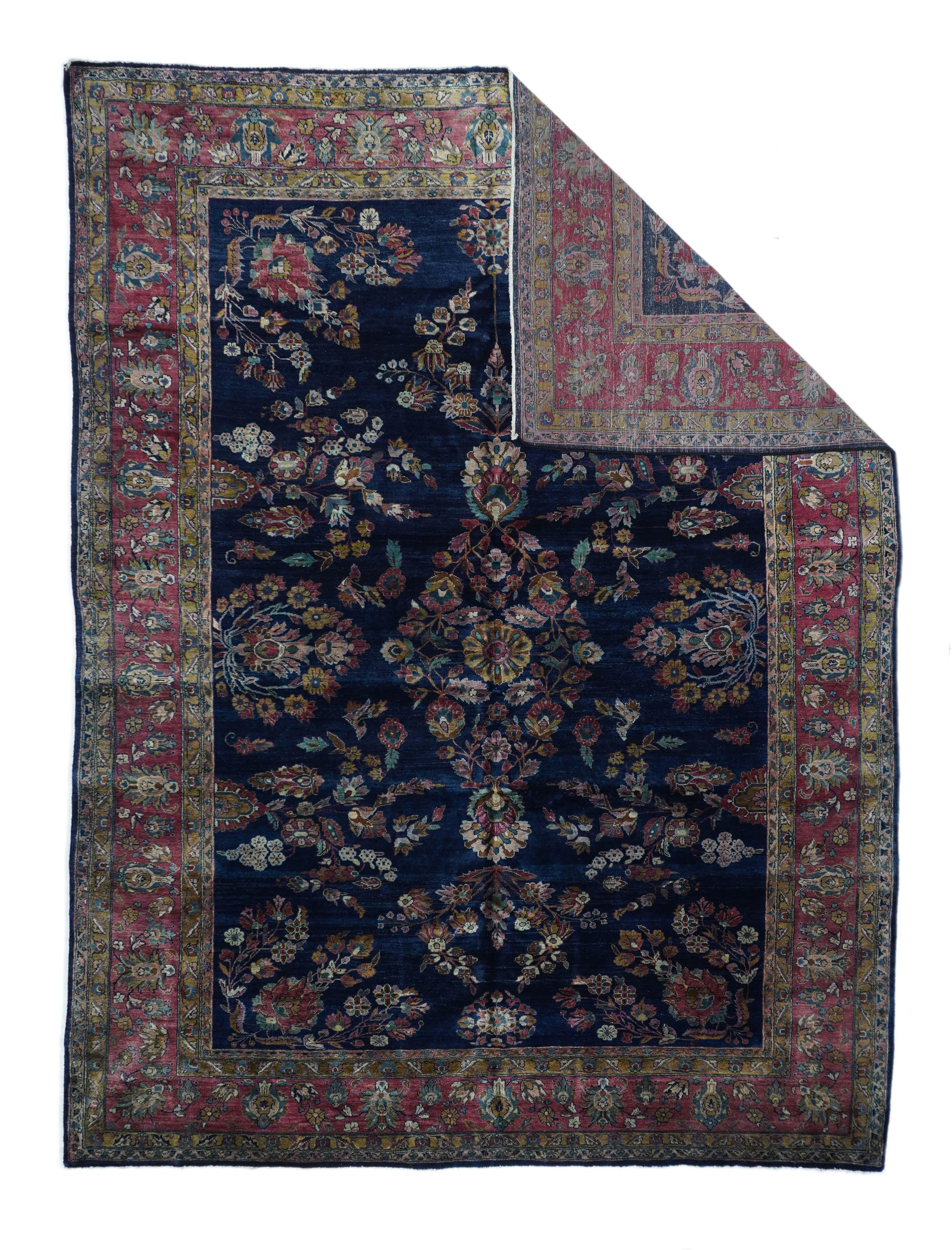 This C. 1920 carpet attributed to Mohajeran village in the Sarouk/Sultanabad/Arak area, shows a deep indigo field with various flower sprays and side palmettes, in shades of teal, straw cream and red. Mulberry red border with two palmette types in