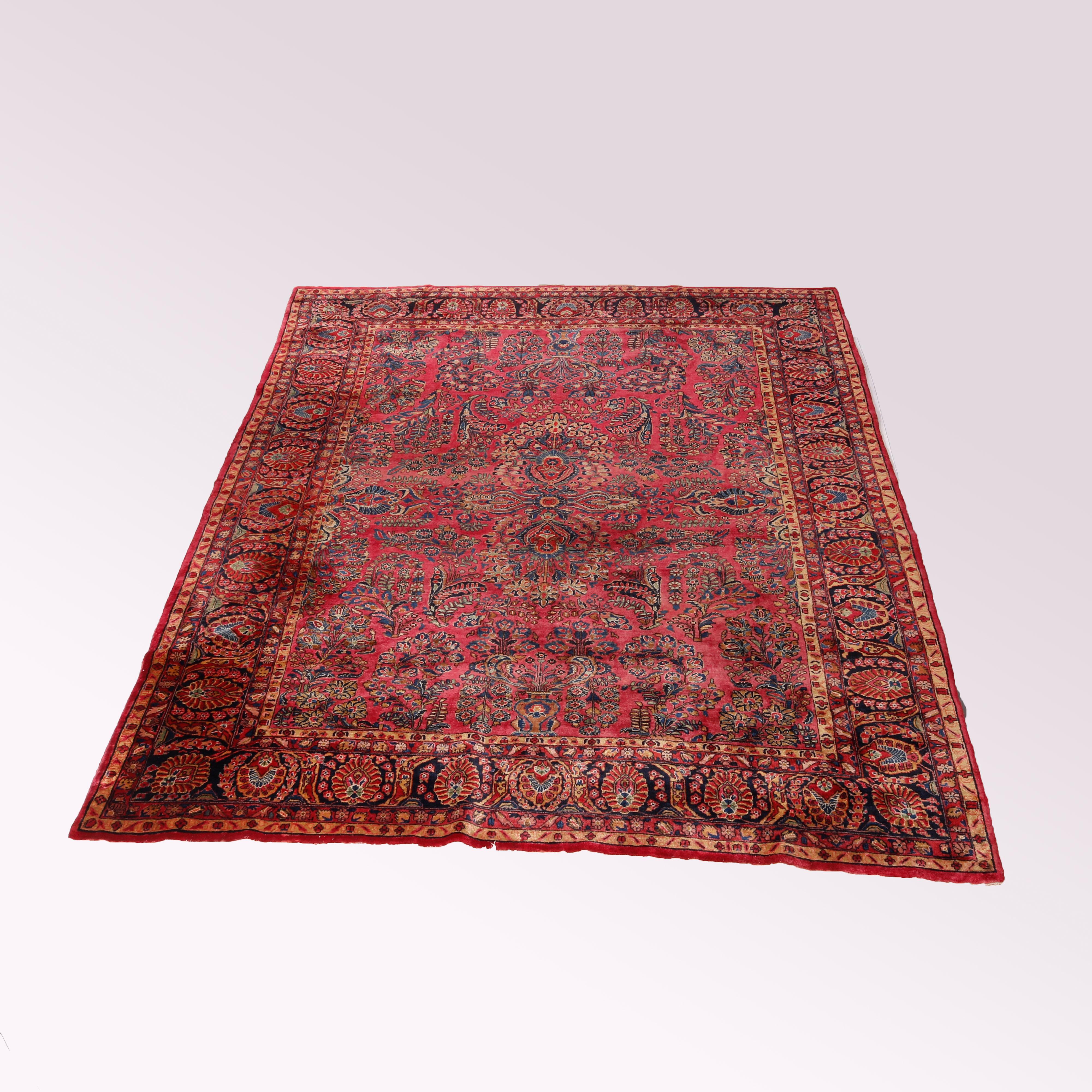 An antique Persian Sarouk oriental large carpet offers wool construction with floral and foliate pattern on red ground, c1930

Measures - 136''L x 102''W x .5''D.

Catalogue Note: Ask about DISCOUNTED DELIVERY RATES available to most regions within