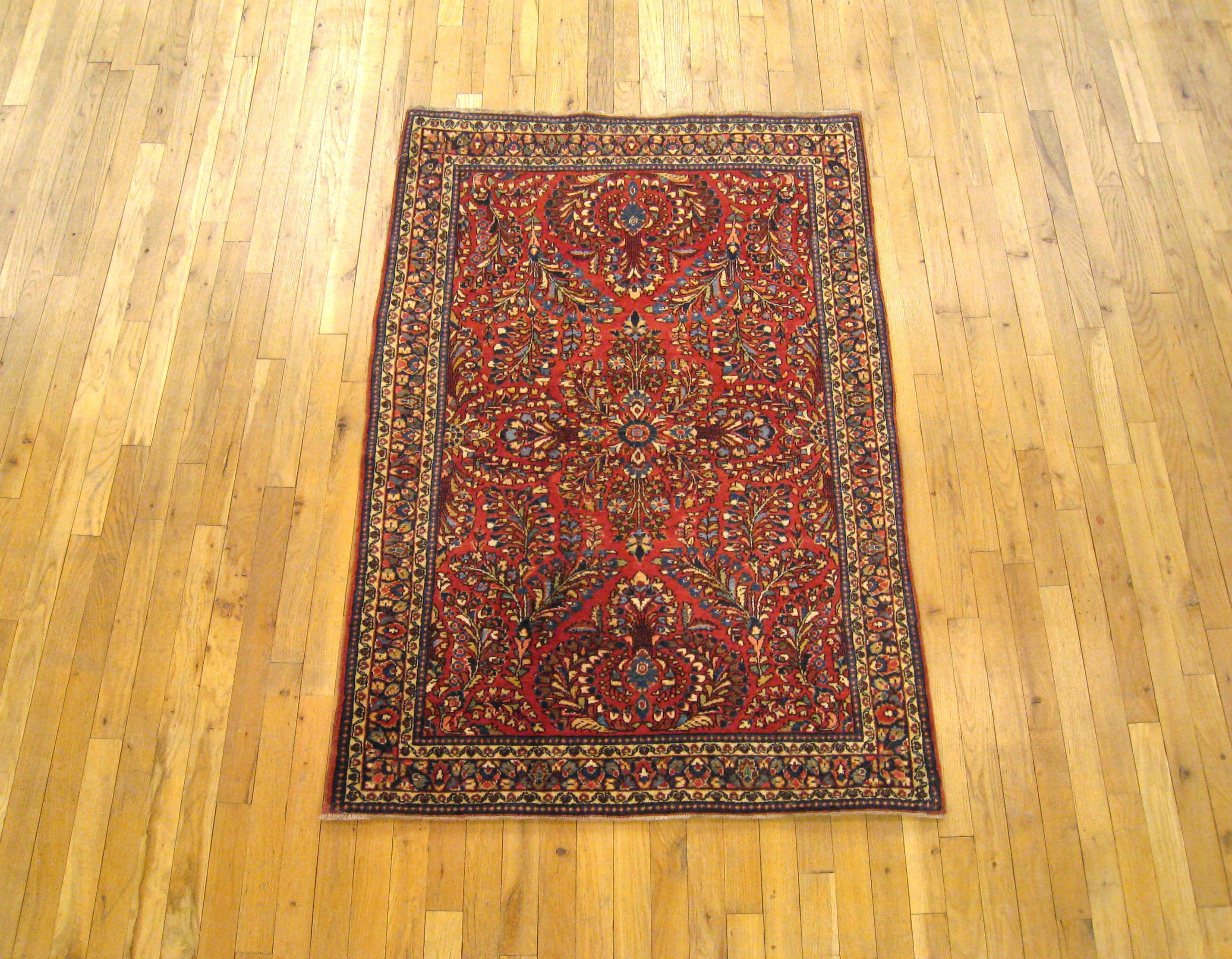 An antique Persian Sarouk oriental rug, circa 1920. Size 5'0 x 3'3. This delightful hand knotted Persian rug is characterized by an elaborate floral design in the red central field, which is enclosed within a scrolling foliate blue border. Composed