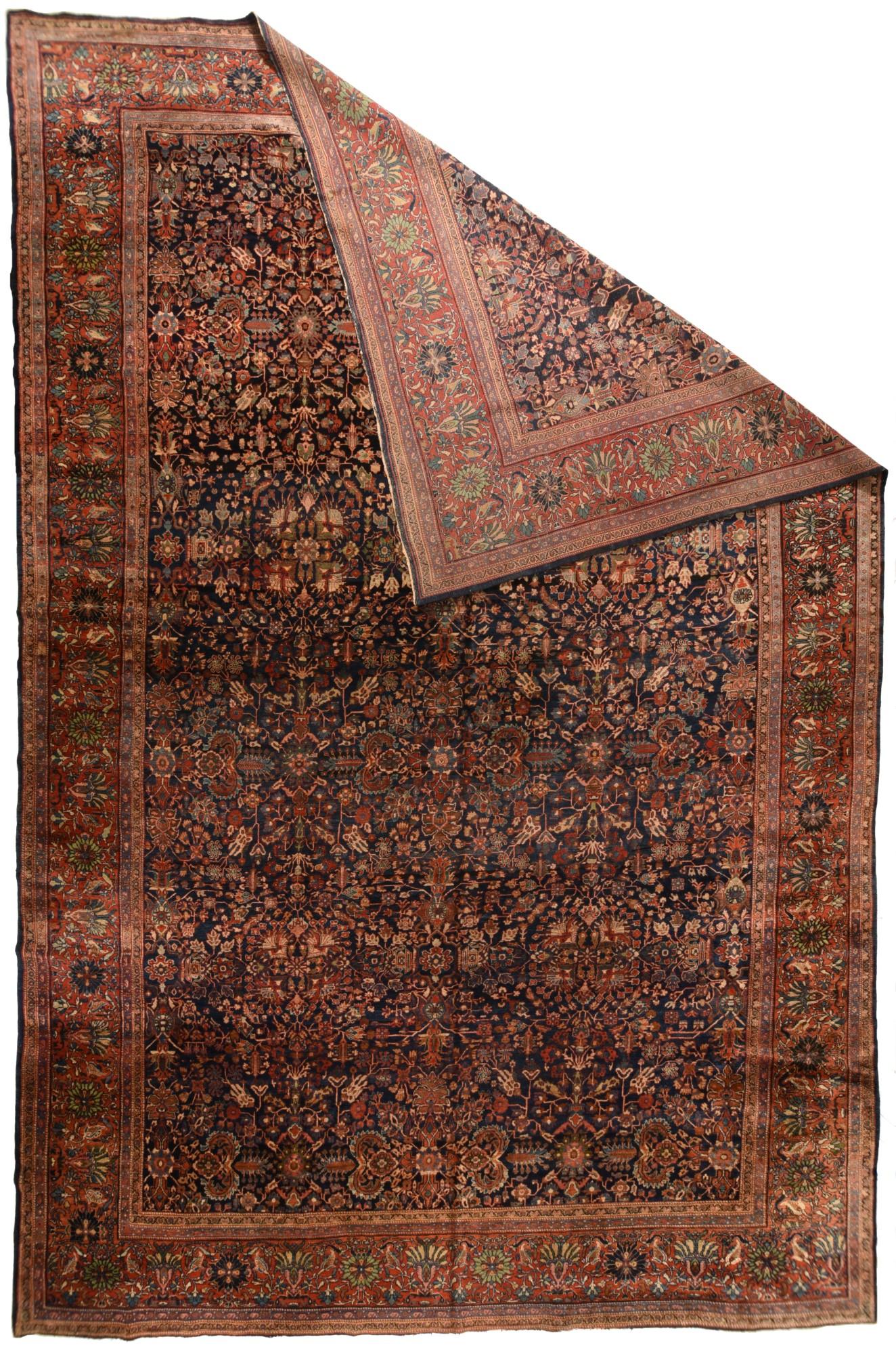 This well-woven, cotton foundation Central Persian city carpet presents a deep navy indigo field with a dense cover of rosettes, palmettes, flowering stems, angular branches and sharply curved barbed bitonal leaves. Saturated red border with
