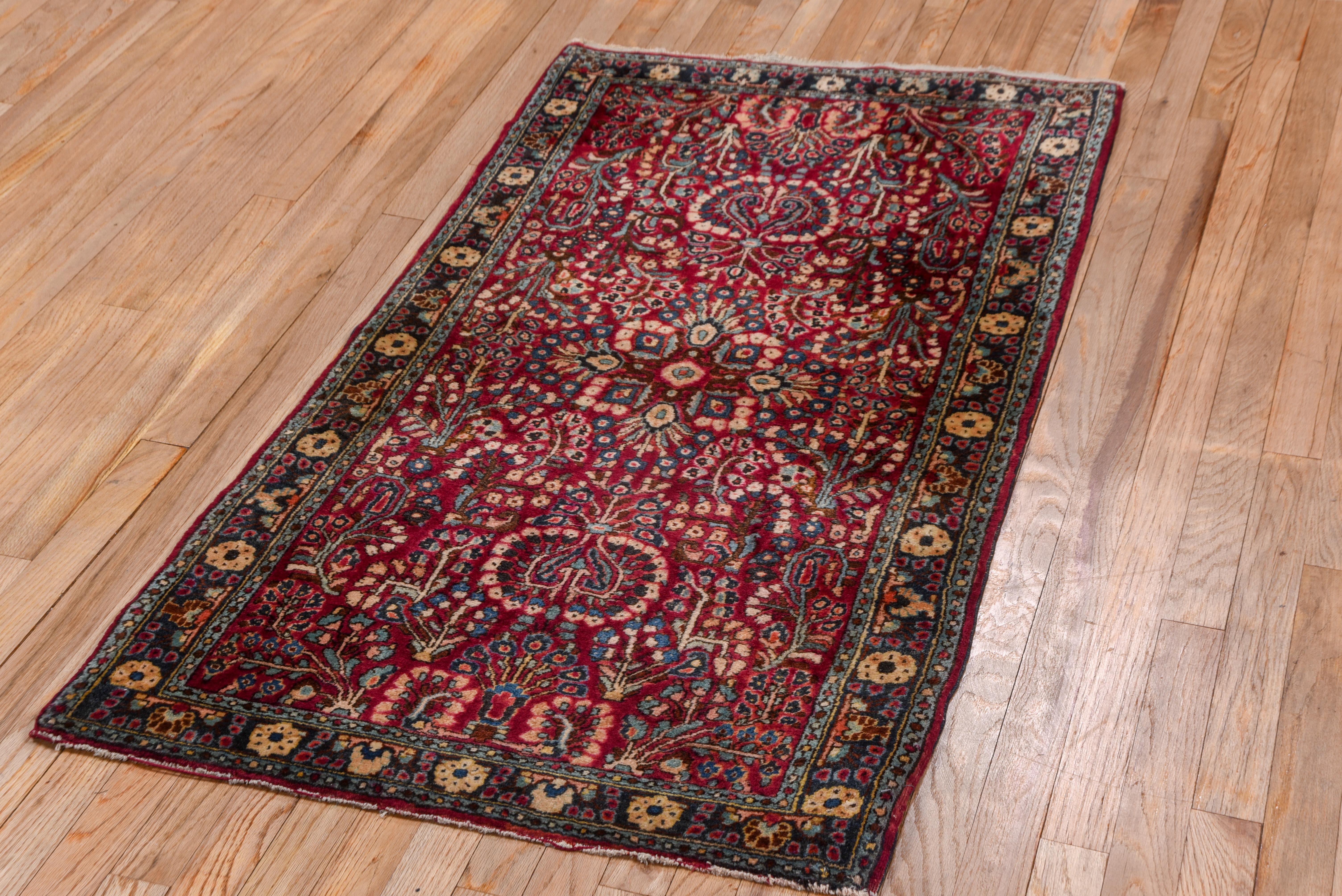 The cardinal red field of this leathery, well-woven West Persian small rustic scatter shows the characteristic 
