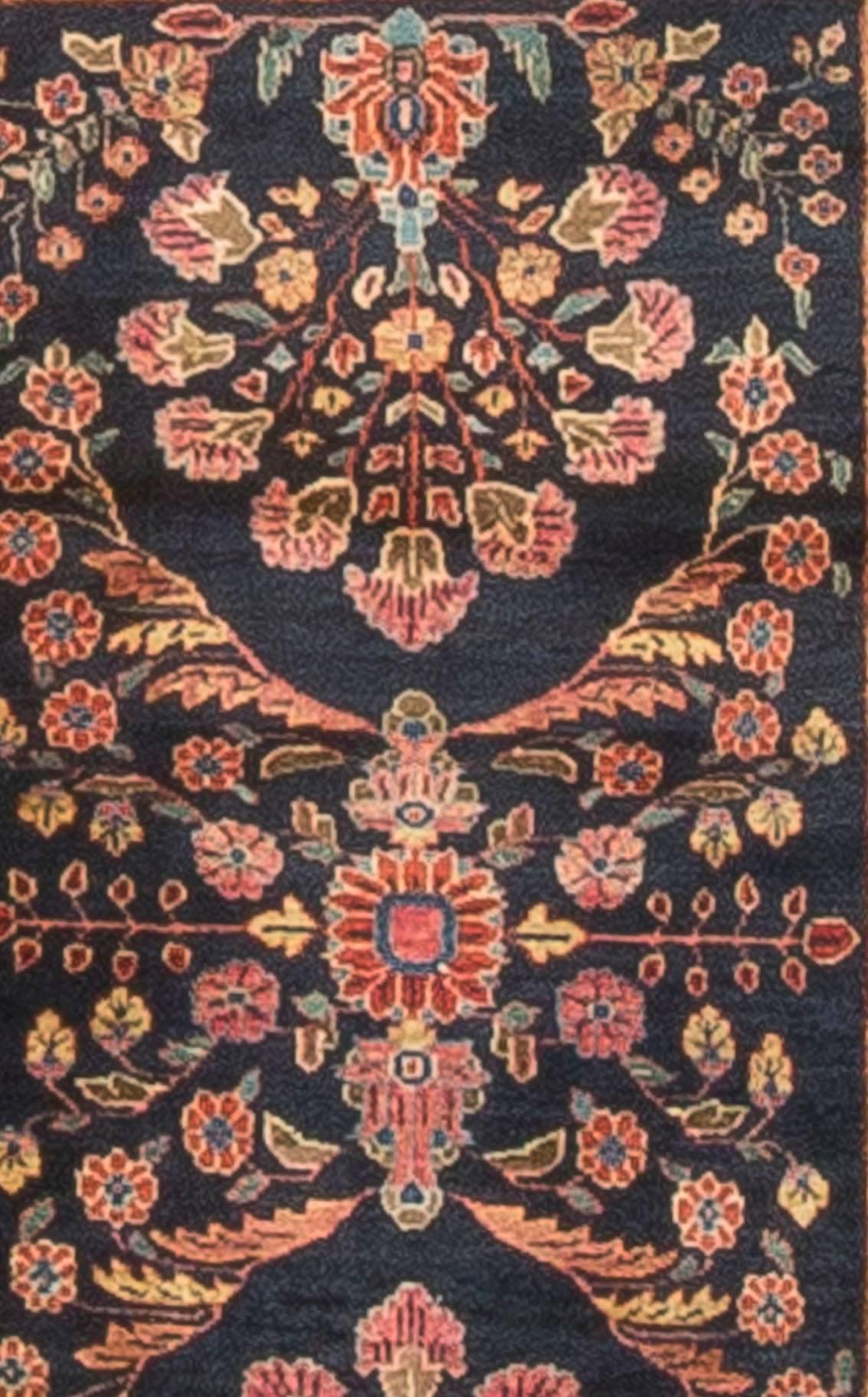 The deep navy field in this antique Persian Sarouk handwoven rug has a marvelous display of flowers sitting at either end of the rug in a pale blue vase. The central floral design adds to the overall look of lightness. The main border and two guard