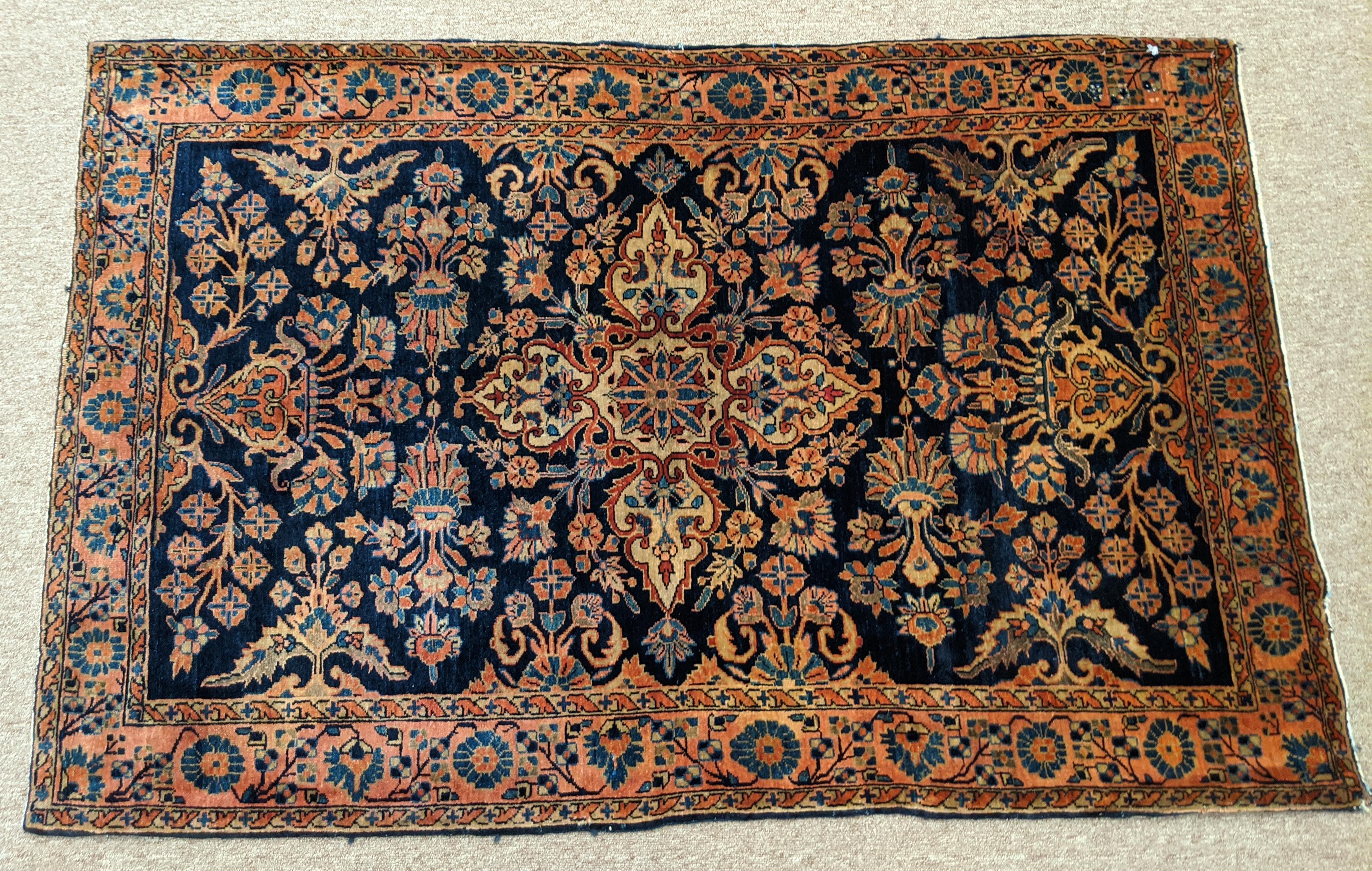 Persian Sarouk with an all-over field design with a navy background and a rust border. The field is decorated with vines, tendrills and flowers in light blue, gold and teal. The wool is so soft that it feels like silk. It is a 3-4x5-1 and is circa