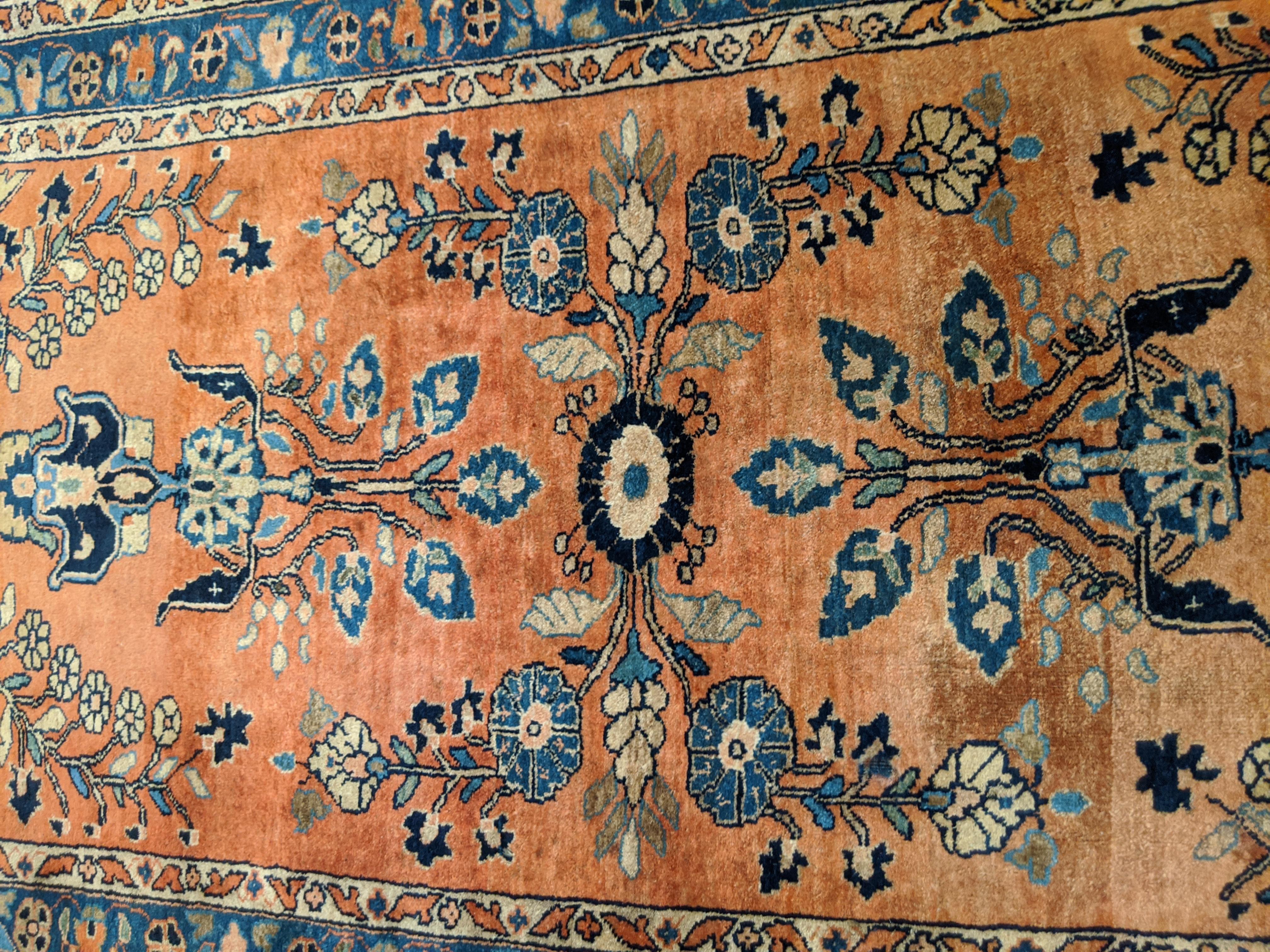 Persian Sarouk with an all-over field design with a rust background and a navy border. The field is decorated with vines, tendrills and flowers in light blue, gold and teal. The wool is so soft that it feels like silk. It is a 2-9x5 and is circa