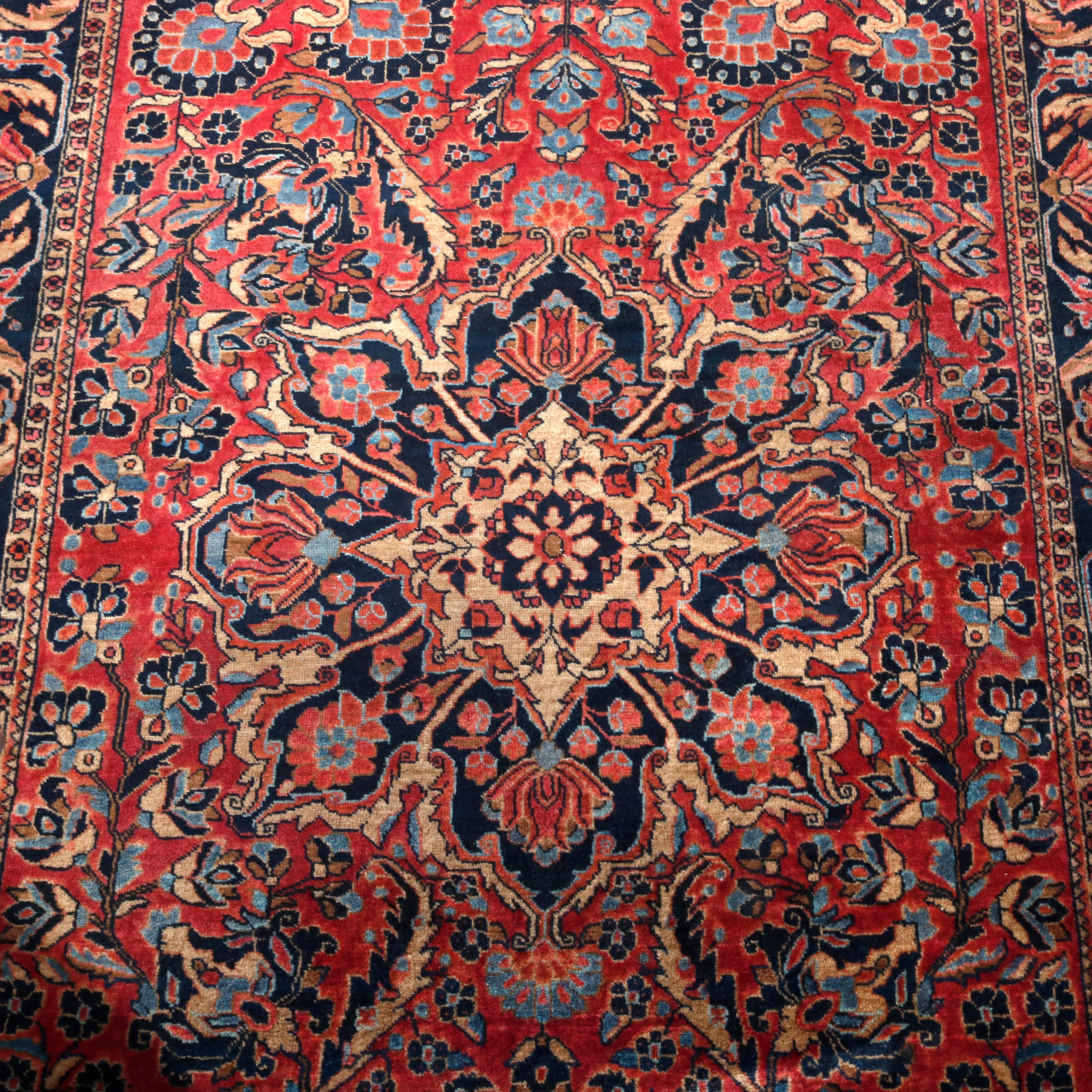 An antique Persian Sarouk oriental rug offers wool construction with central floral medallion and all-over floral and foliate design on red ground, circa 1920.

Measures: 81