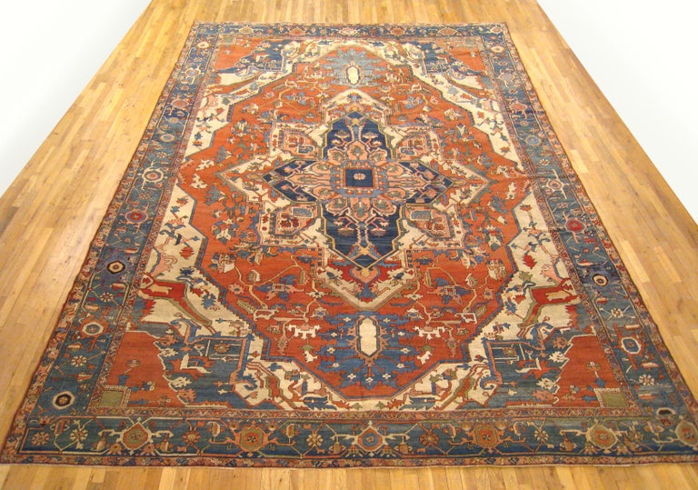 An antique Persian Serapi oriental carpet, size 15'0 x 10'1, circa 1890.  This handsome hand-knotted carpet features a stylish central medallion anchoring a soft red field, surrounded by a layer of ivory, and a medium blue outer border.  Woven with