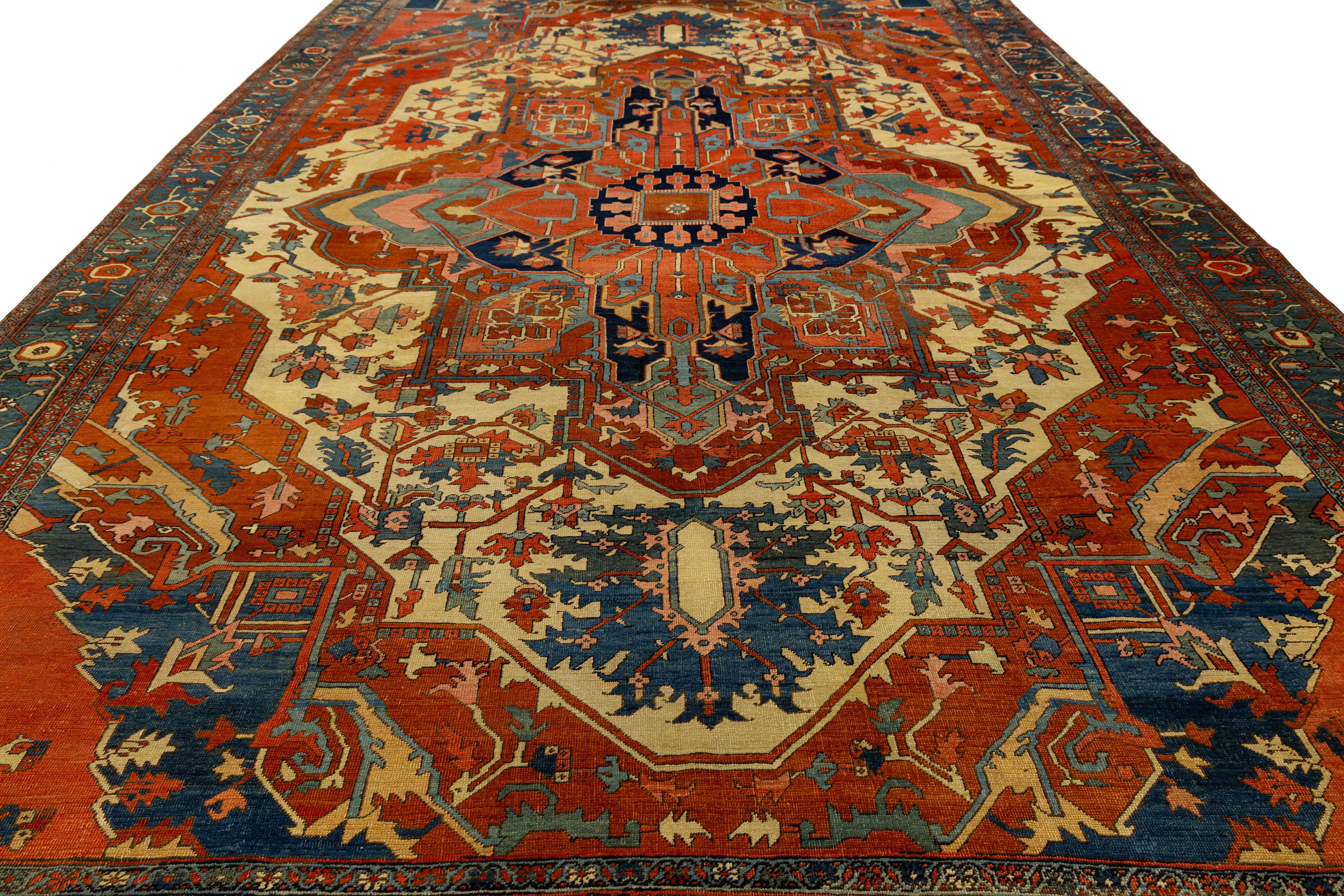 This hand-knotted antique Serapi rug showcases a striking central medallion and angular floral motifs in rich tones of red, navy, and ivory. Woven from high-quality wool, its bold geometric layout and tribal elegance reflect 19th-century Persian