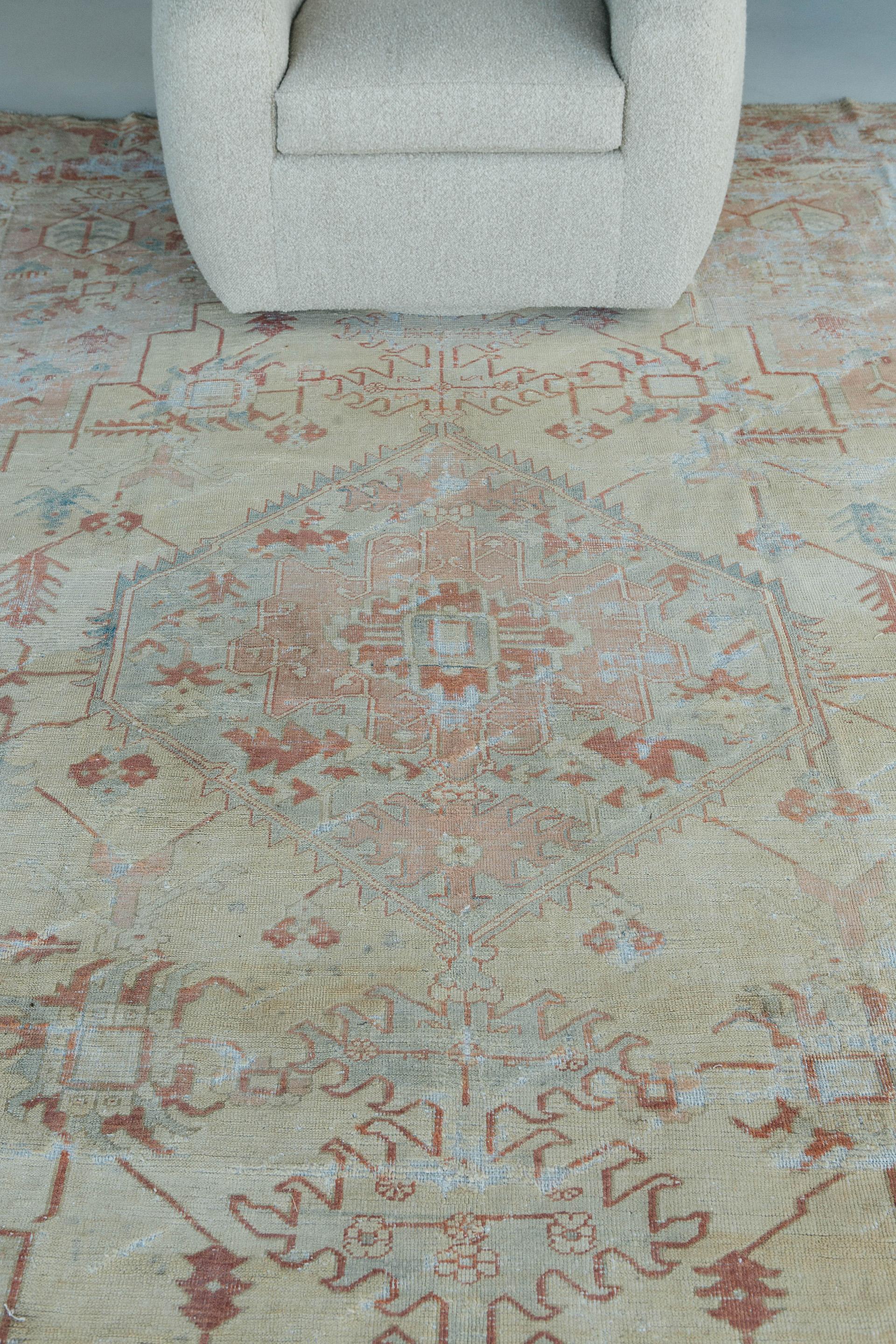 Pale gold, rose and coral with soft celadon accents set a quietly sunny mood in this ethereally-aged antique Serapi. A highly stylized geometric center medallion anchors the rug and is surrounded by numerous geomorphic floral patterns. Stepped