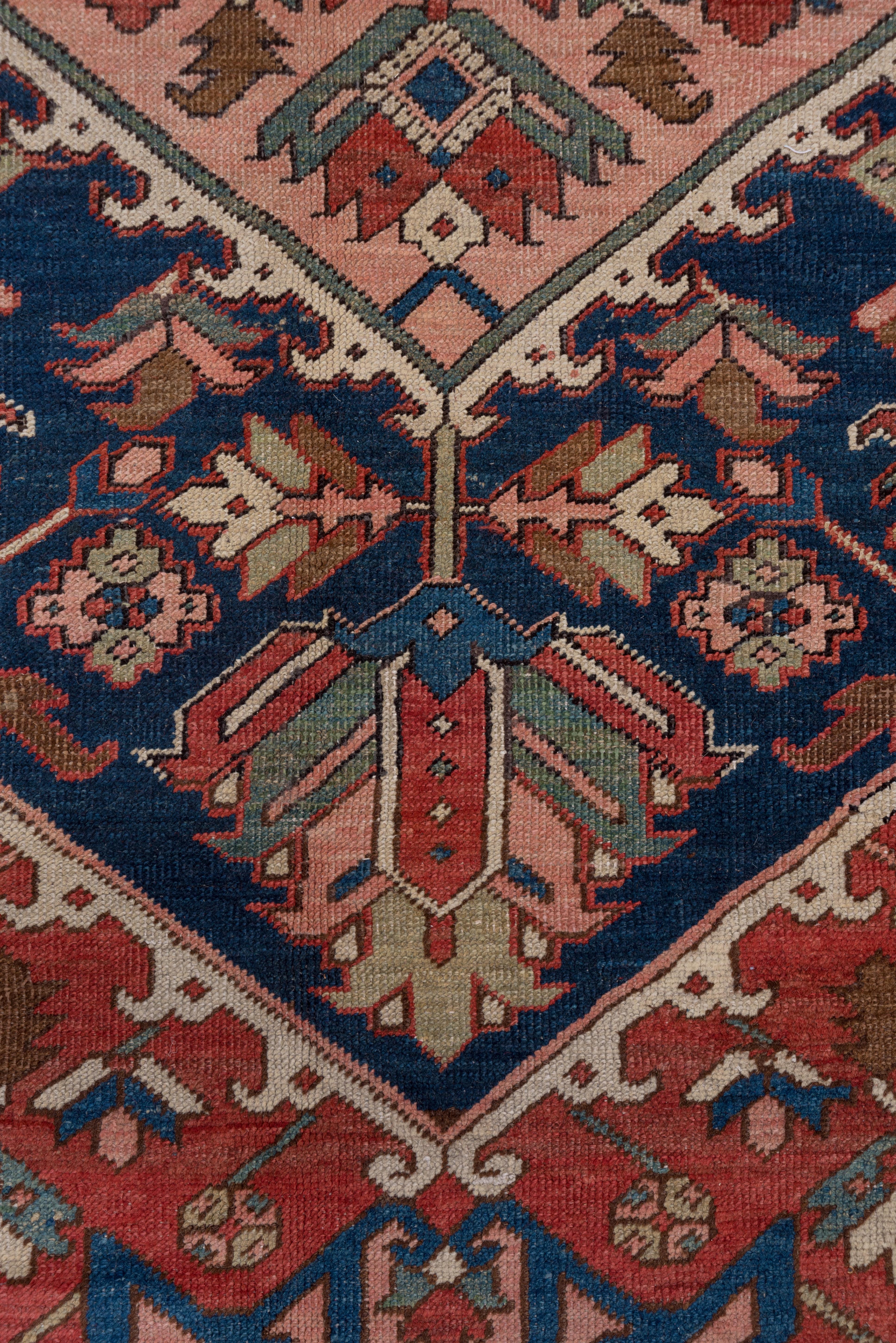 This high Serapi quality NW Persian rustic carpet in all natural dyes shows broad, conjoint, flower-filled cream corners, setting forth the tomato red field with an inner hook fringe and a dark blue lozenge medallion with a sub-medallion sprouting