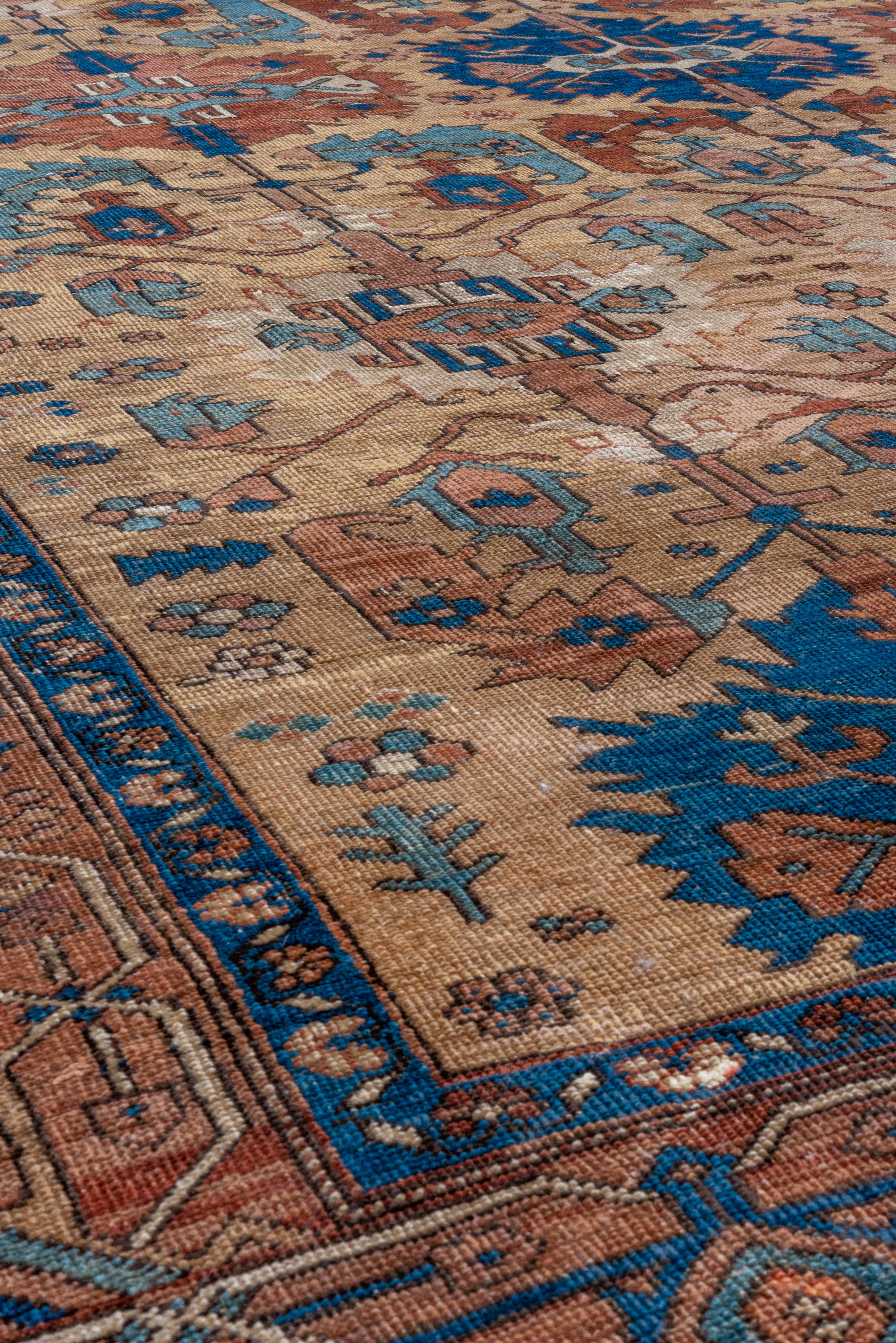 The camel-tan field presents a three- column design of serrated, bold oval palmettes in rust and cerulean blue, with smaller stepped ecru medallions and sharply bent pale blue or rust large leaves. Abrashed rust reversing semi-geometric turtle