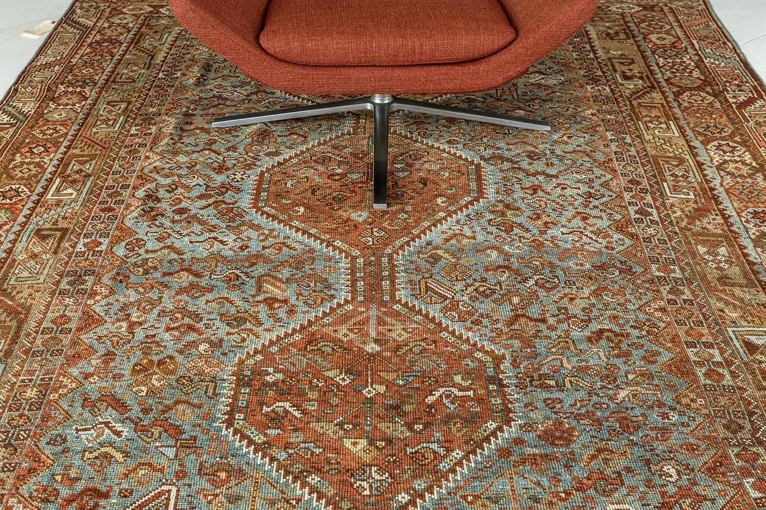 This sophisticated Antique Persian Shiraz rug from Persia features a beautiful natural wool pile. It is adorned with cinnamon, saffron, and earthy tone colors that ensembles motifs, florid elements, and symbols. Series of three central medallions,