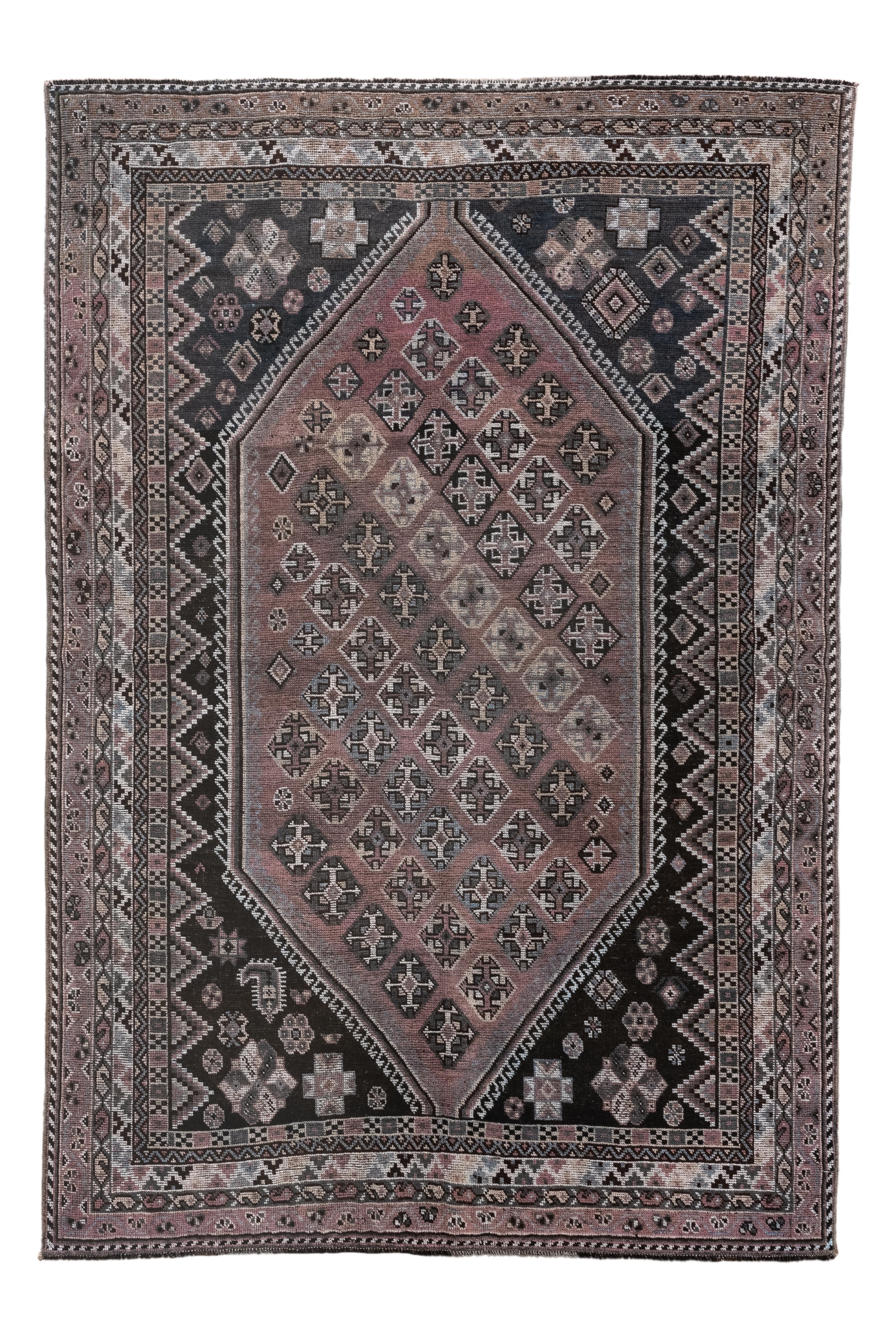 Dieser antike persische Shiraz-Teppich, der um 1920 gewebt wurde, zeigt ein kühnes, längliches Rautenmuster  Medaillon, das ein Gitter aus Stammesmotiven in gedämpften Rosa-, Kohle- und Grüntönen umschließt  Elfenbein. Die detaillierte Umrandung