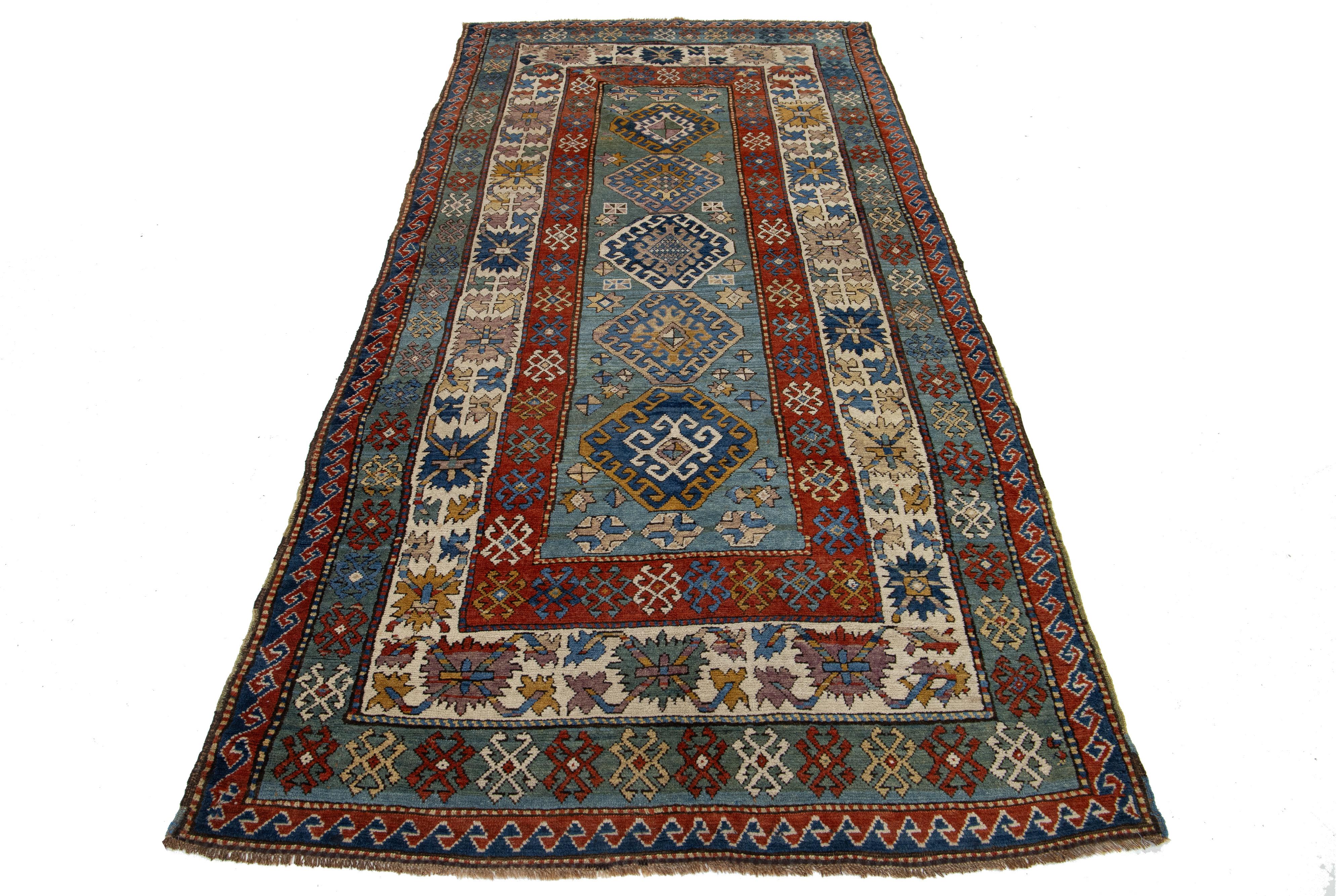 Dieser Wollteppich zeigt ein Stammesmuster in Braun und Beige,  und roten Akzenten auf blauem Hintergrund, inspiriert von persischen Schirwan-Mustern.

Dieser Teppich misst 4'6
