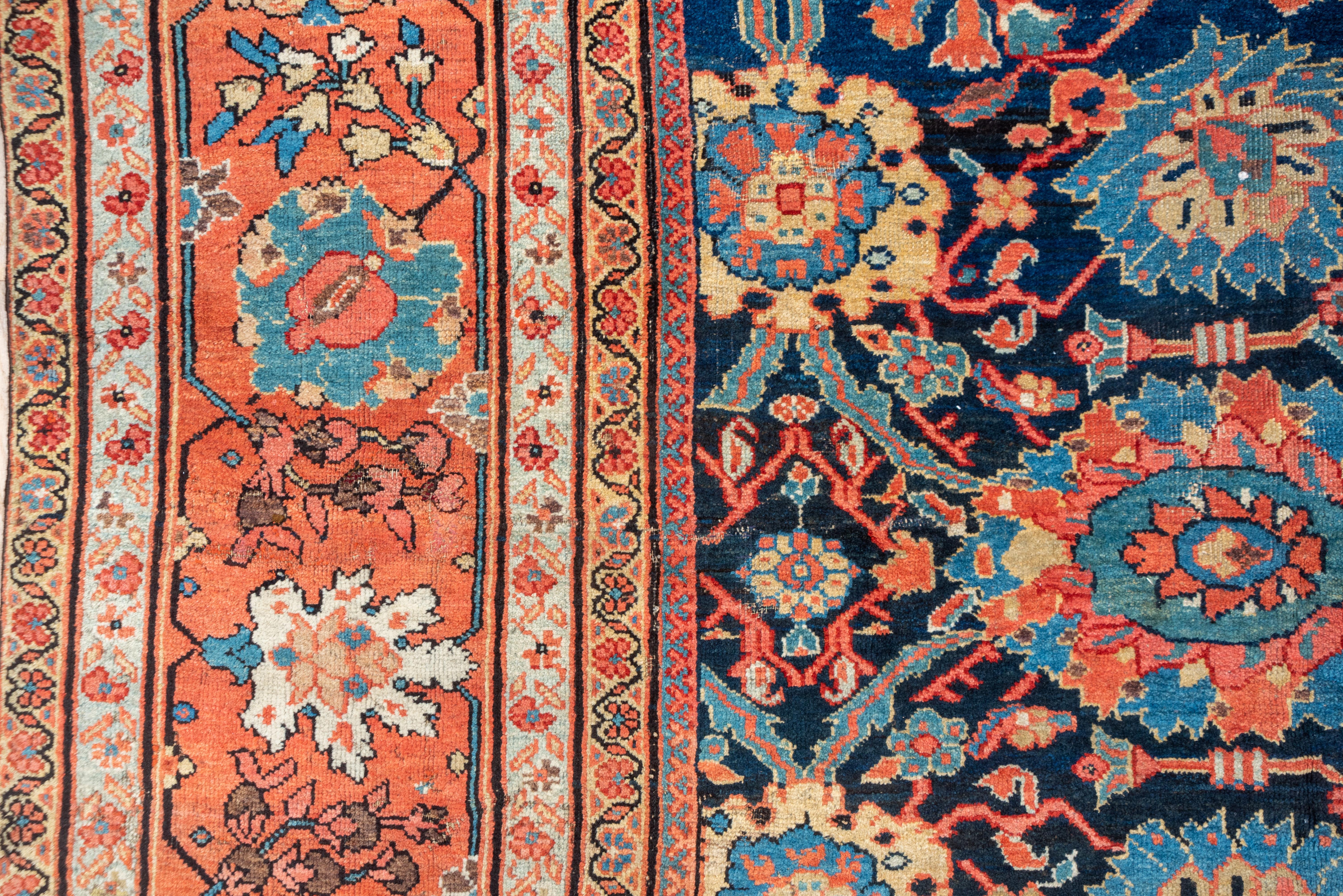This magnificent west Persian village carpet shows a deep indigo navy field supporting an all-over pattern of ragged and smoothly oval palmettes, both lazy and erect, all detailed in lighter blues, straw, teal, green and light rose.