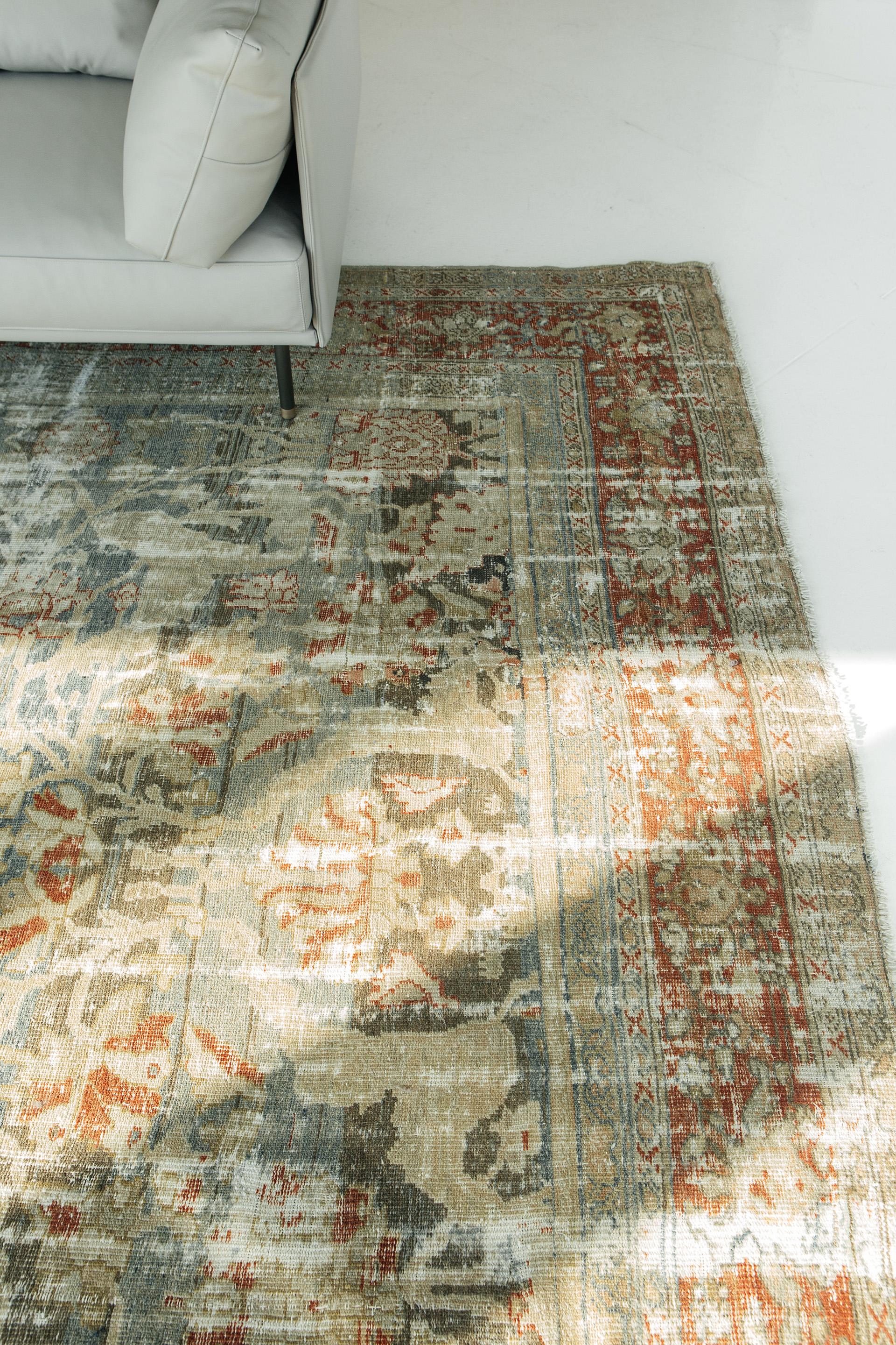 This distressed antique Sultanabad features taupe and varied indigo ground tones, with a barn-red main border and detailing, and tan and ivory accents throughout. The distribution of wabi-sabi distressing creates a pleasing contrast to the rug’s