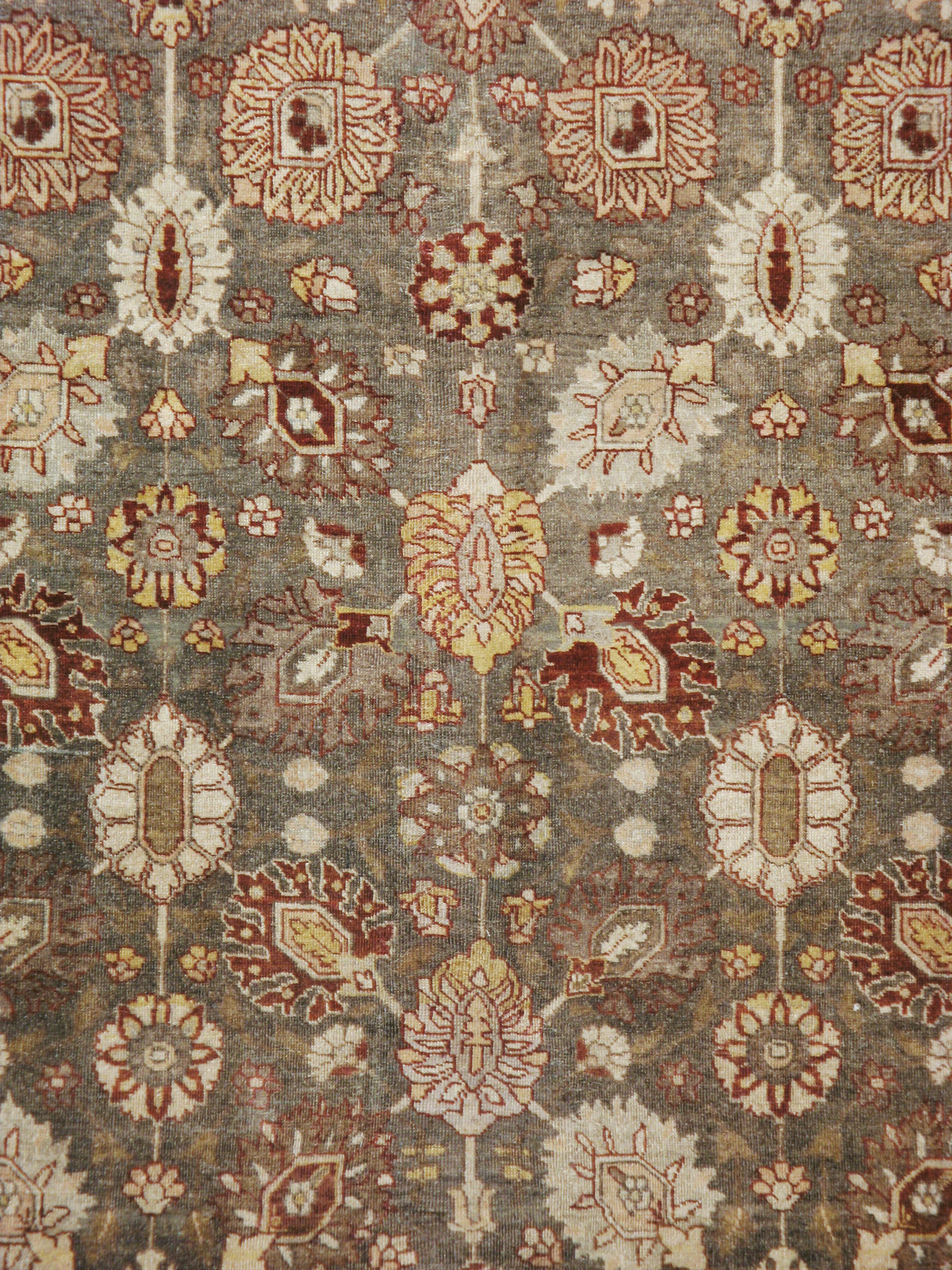 An antique Persian Tabriz carpet from the early 20th century. This modified “Vase carpet” pattern features five vertical axes organizing erect and slanted palmettes on the khaki brown field. The rust main border of palmettes and arrays of nine