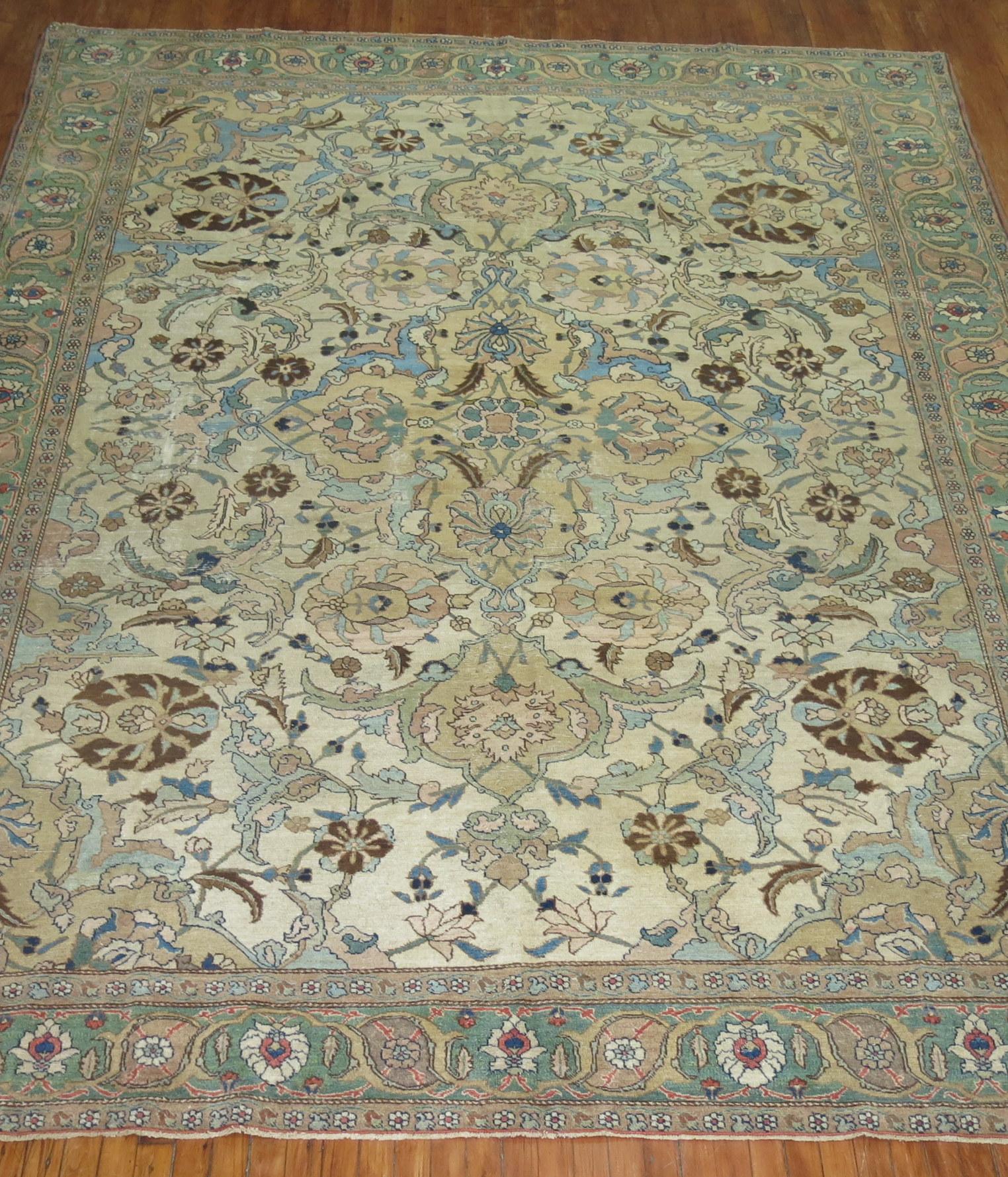 An early 20th century Persian Tabriz rug with light blue and brown dominant accents on an off white field, green border.

Measures: 9' x 12'3''.