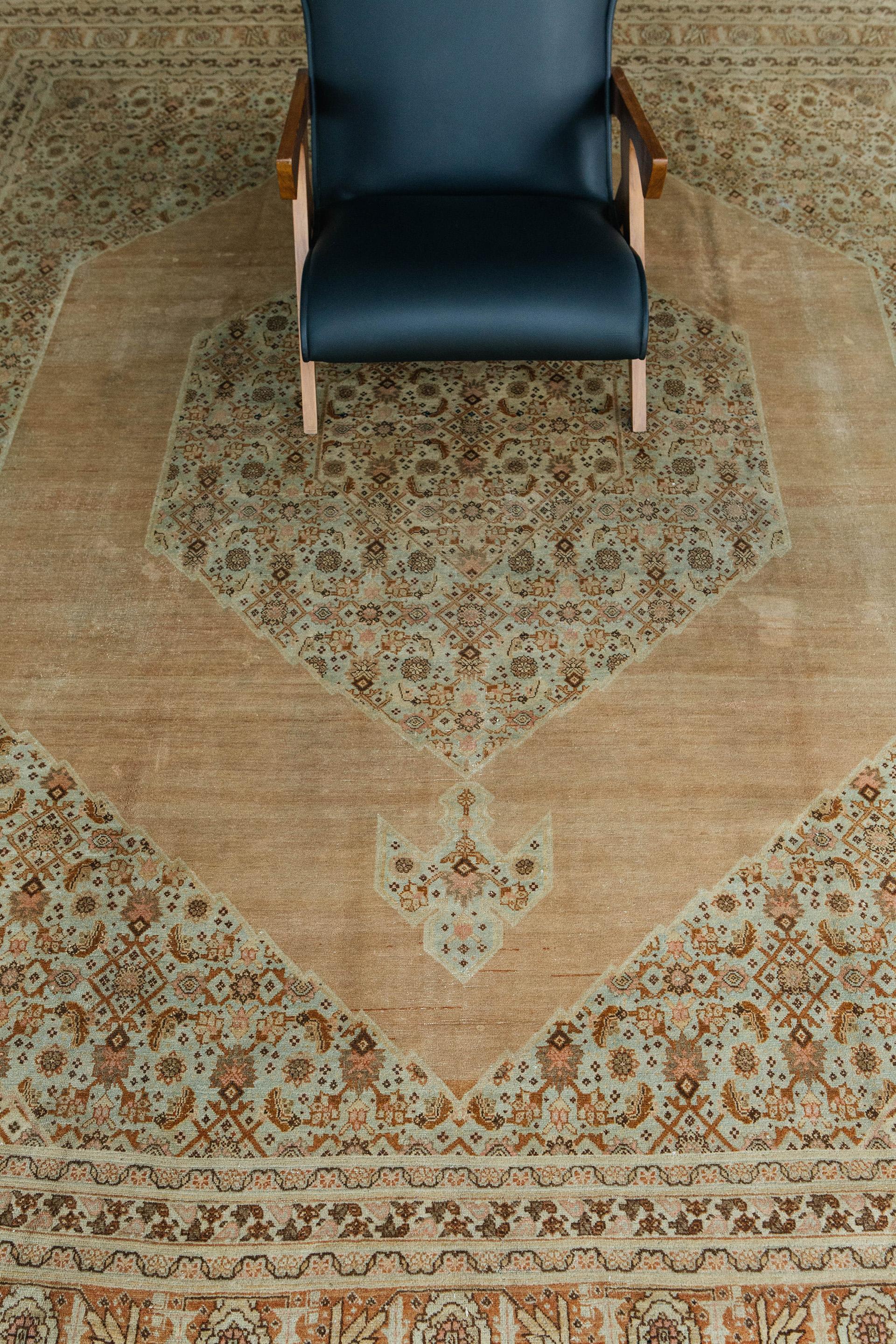 Antique Tabriz in soft camel with ivory, tan and celadon, and accents of browns, rose and umber tones. The composition features a large hexagonal medallion with geometric pendants and corner-pieces. These areas have a small-scale herati pattern with