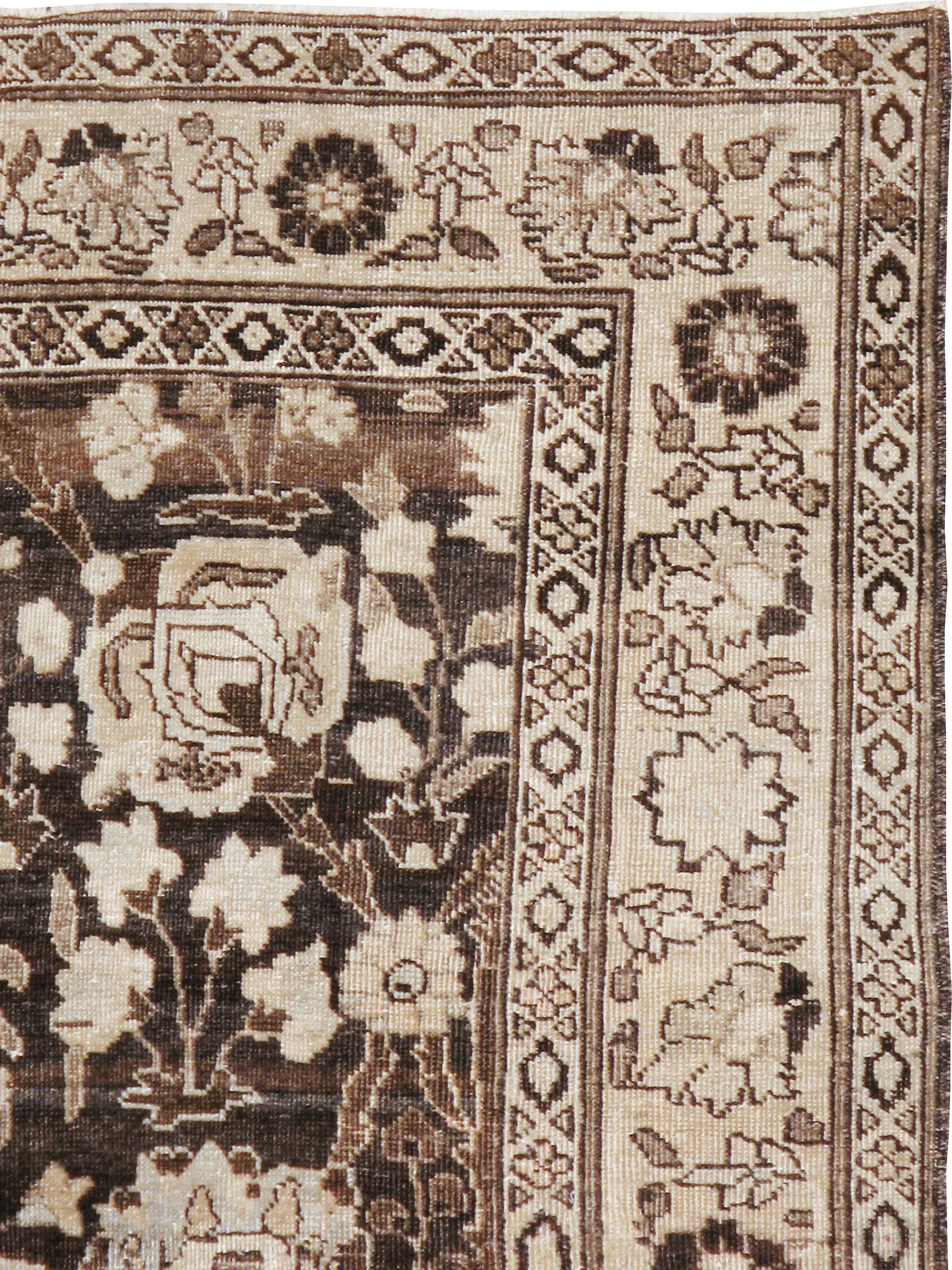 An antique Persian Tabriz rug from the early 20th century. A vase with a flowering prunus spray is a standout feature of the one-way palmette and garden flower pattern on the charcoal brown ground of this NW Persian city scatter. This is really a