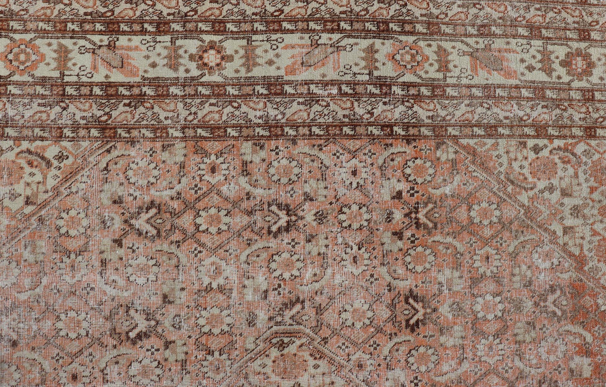 This antique Persian Tabriz rug features an all-over, sub-geometric floral design rendered in off white, orange and brown tones. A complementary, multi-tiered border encompasses the entirety of the piece; making it a marvelous fit for a wide variety
