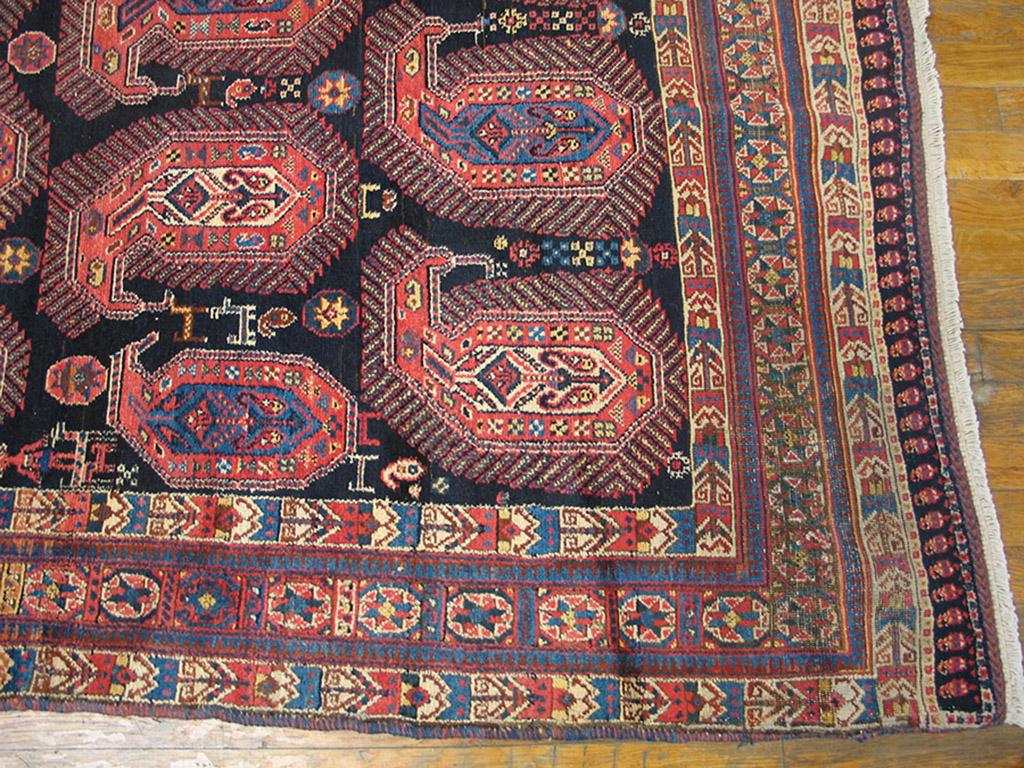 Botehs of all sizes fill the navy blue field of this c. 1900 antique rug,. but especially giant fringed cones facing left and right. A few small animals add to the rustic informality of this carpet. The inner and outer ivory borders with geometric