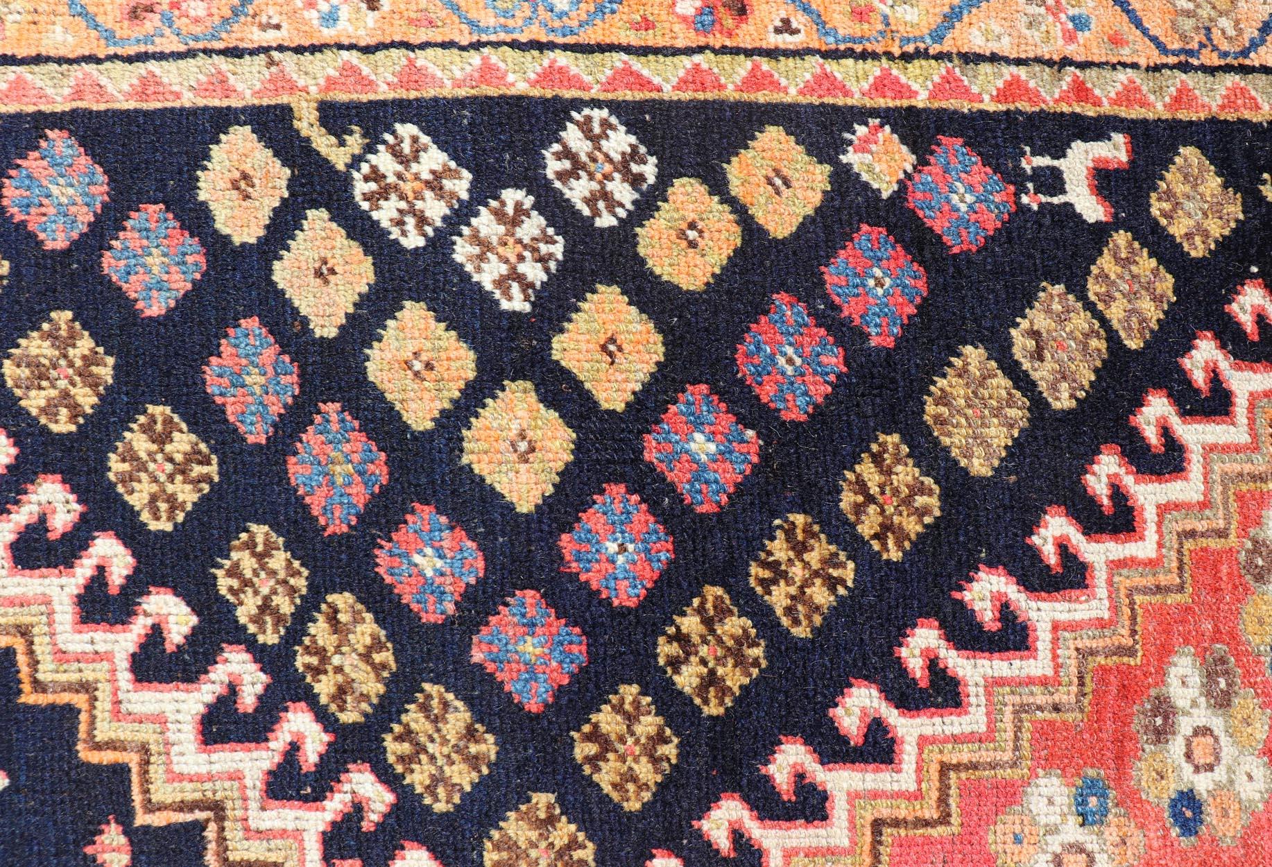 Dieser antike persische Shiraz-Teppich ist aus Wolle handgeknüpft und zeigt ein subgeometrisches Stammesmedaillon-Design in mehrfarbigen Tönen. Eine komplementäre, mehrstufige Bordüre umgibt das gesamte Stück und macht es zu einer wunderbaren
