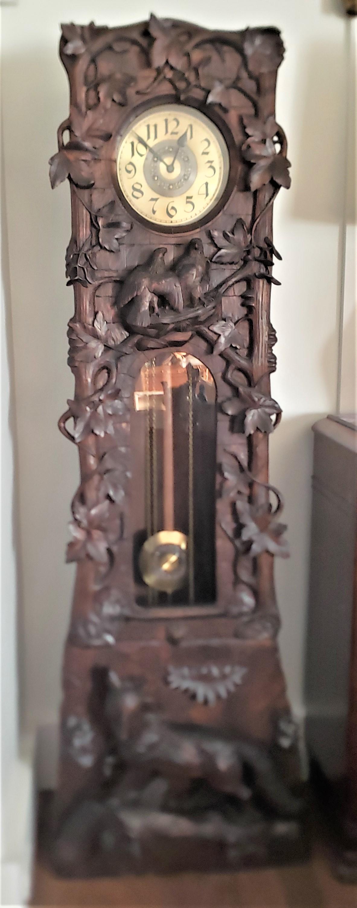 This antique grandfather or longcase clock was done by the renowned Peter Trauffer of Switzerland in approximately 1920 in his signature Black Forest style. The case is composed of walnut which has applied ornately carved leaves along the top of the