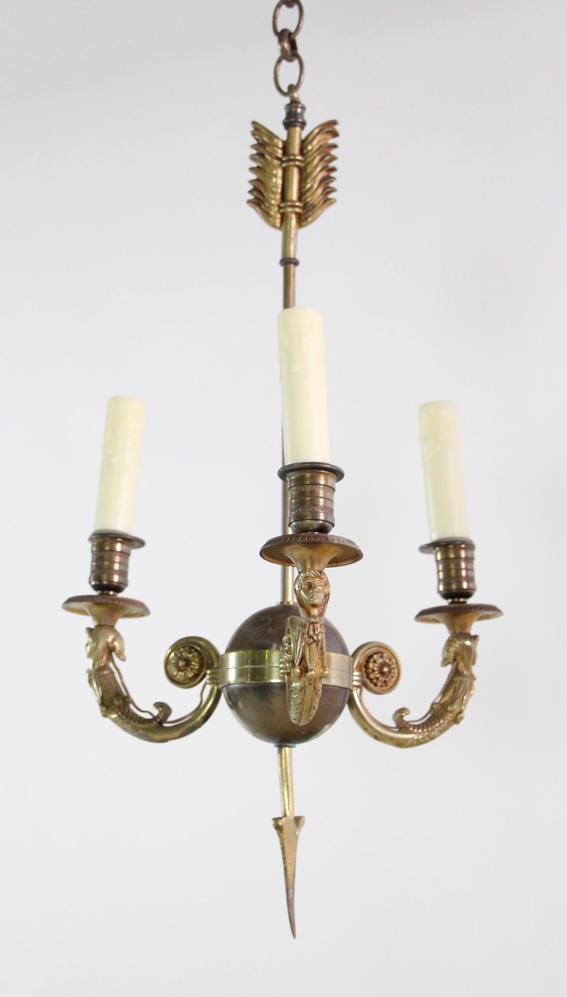 Late 1800s ornate French petite brass three arm chandelier with detailed faces on the arms and arrow feather top. This can be seen at our 400 Gilligan St location in Scranton, PA.
 