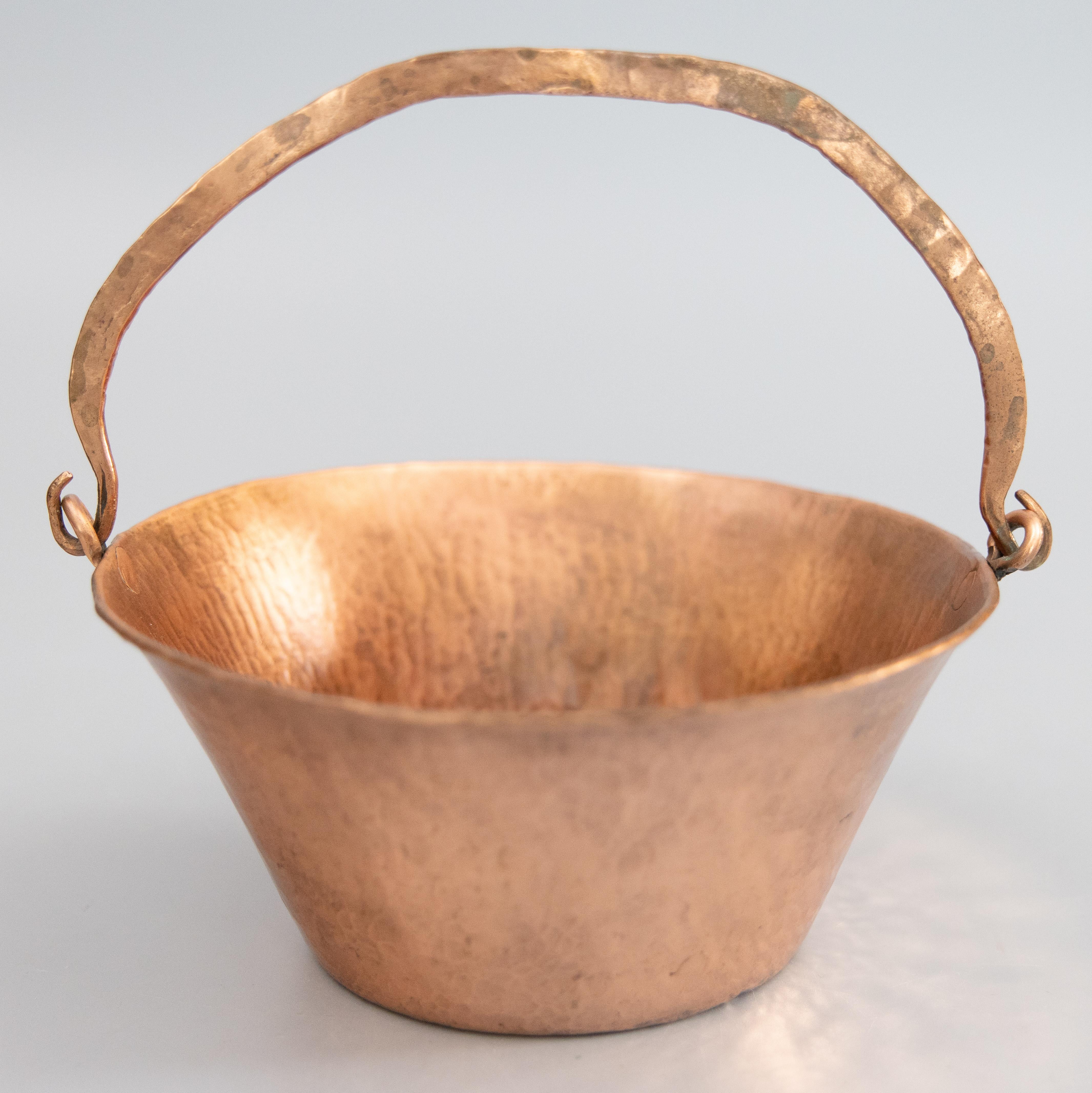 A gorgeous antique early 20th-Century hand-hammered petite French copper planter or hanging basket with a swing handle and a lovely patina. Perfect for greenery or small decorative objects to brighten your kitchen or living space. The height with
