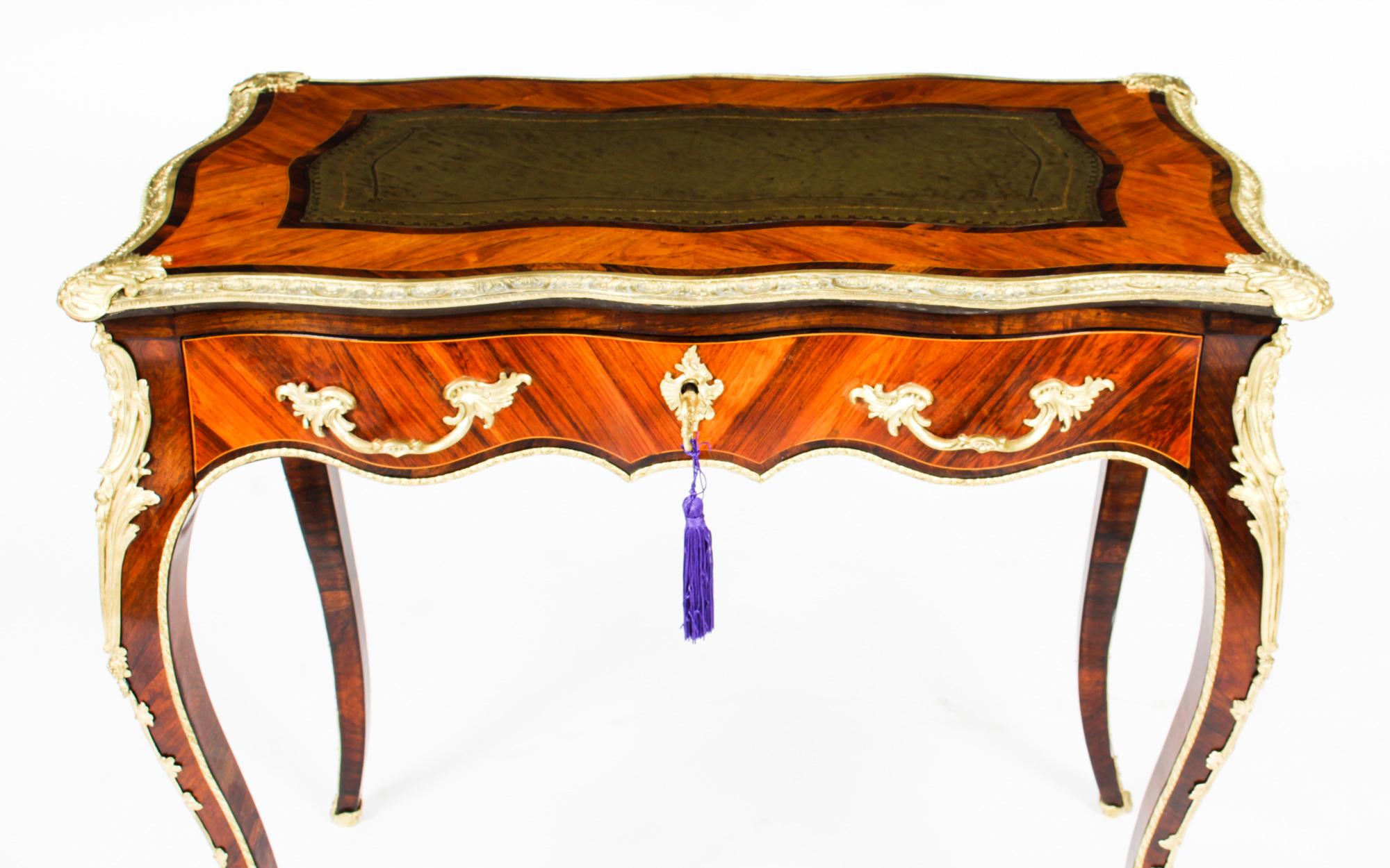 This is an fine and beautiful petite French Louis XV Revival goncalo alves and ormolu mounted bureau plat, circa 1850 in date.
This fantastic bureau plat features an ornate serpentine crossbanded top inset with a gold tooled green leather writing